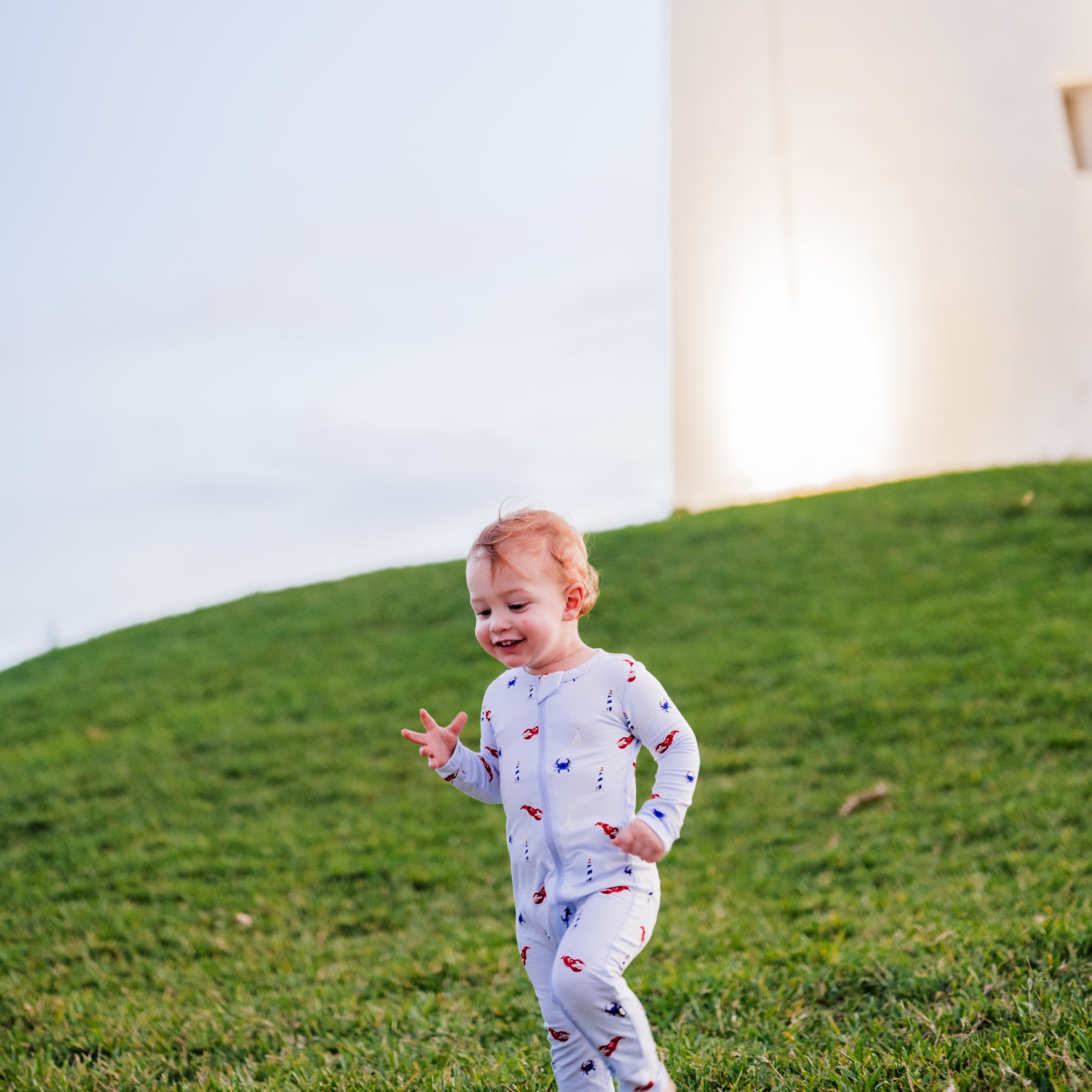 Toddler in Zippered Romper in Harbor on a grassy hill running