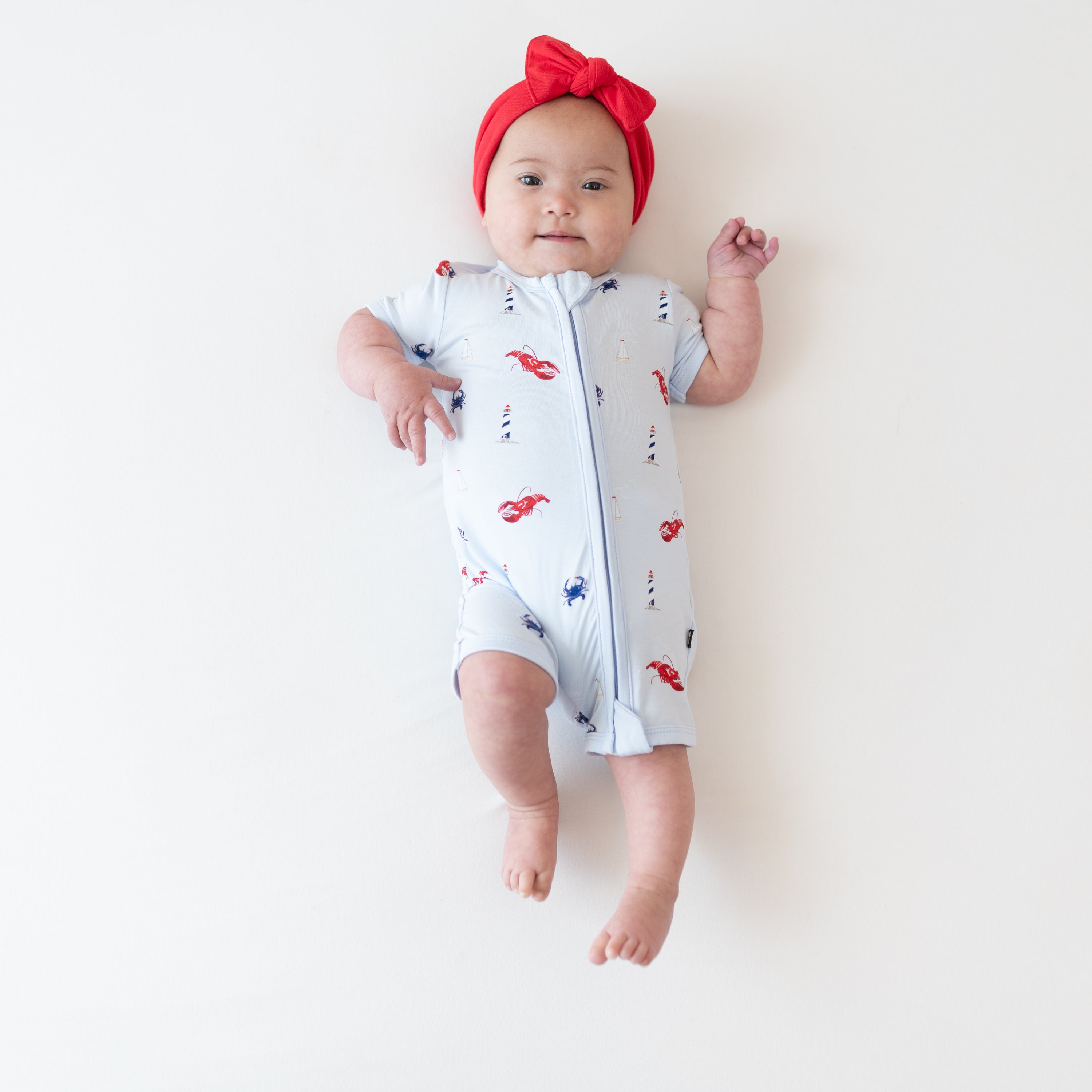 Infant girl wearing the Zipper Shortall Romper in Harbor paired with a Knotted Bow Headband in Cardinal
