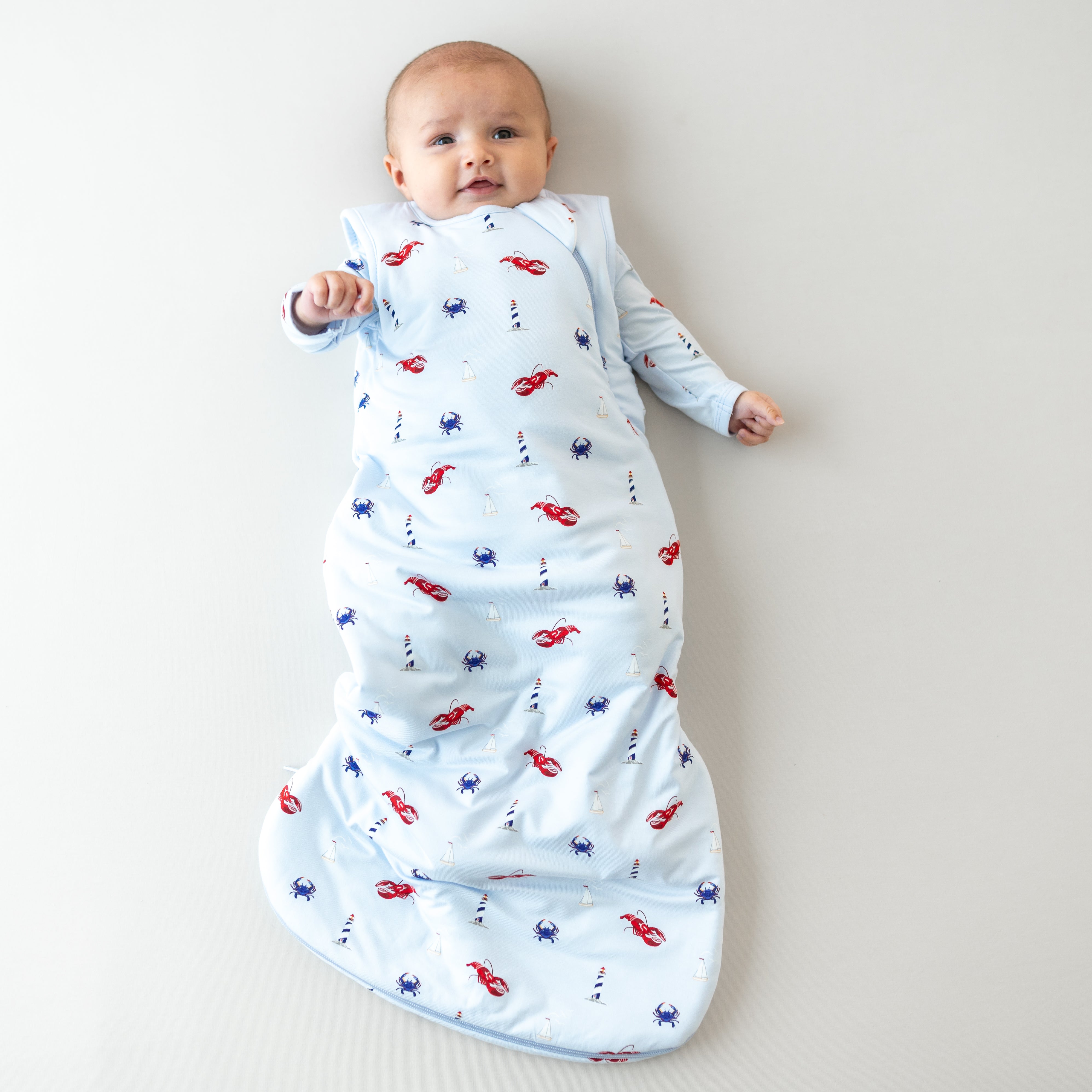 Infant laying down wearing the Sleep Bag in Harbor 1.0 with matching long sleeve romper