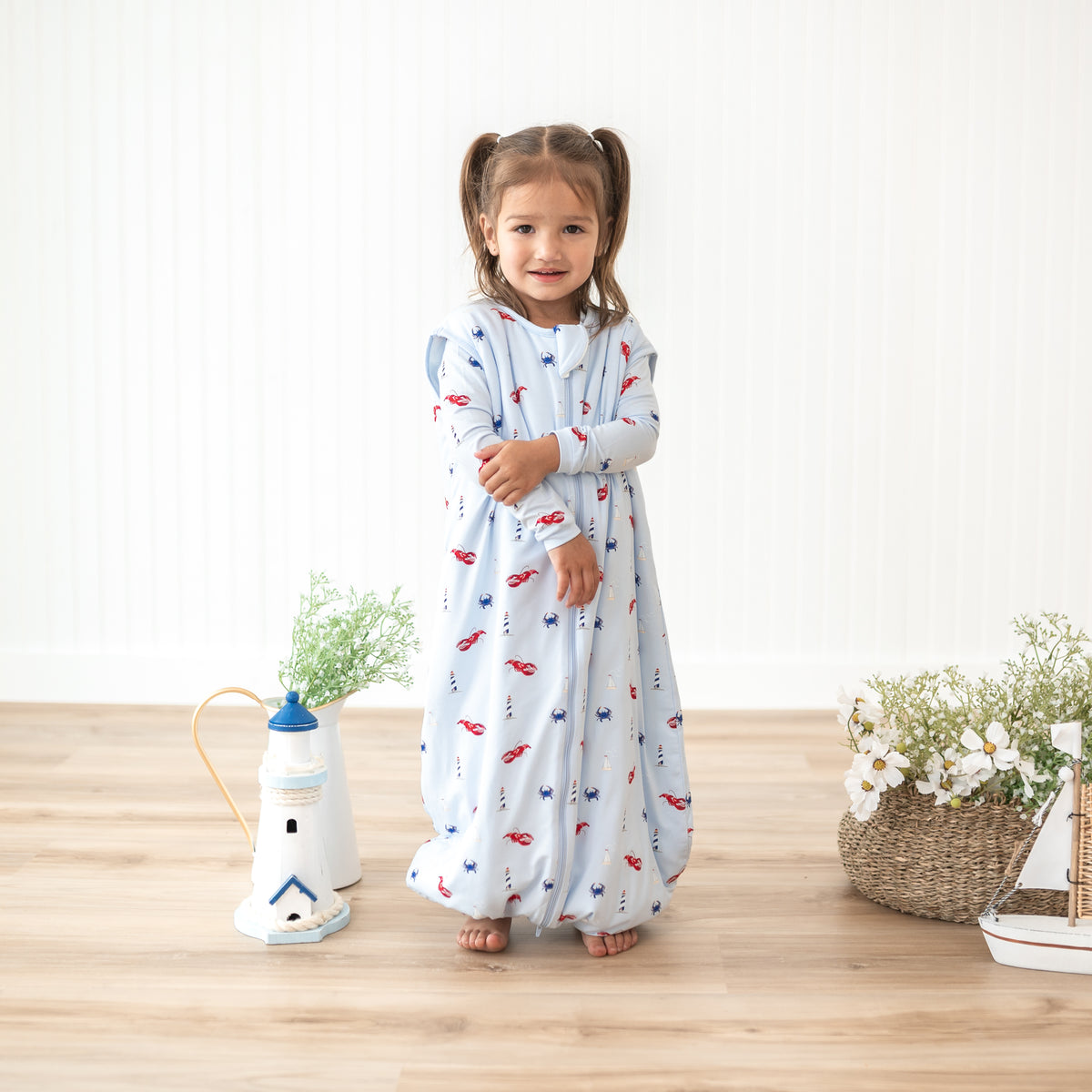 Toddler girl standing beside potted flowers and plants wearing the Sleep Bag Walker in Harbor 1.0 with matching toddler pajamas underneath