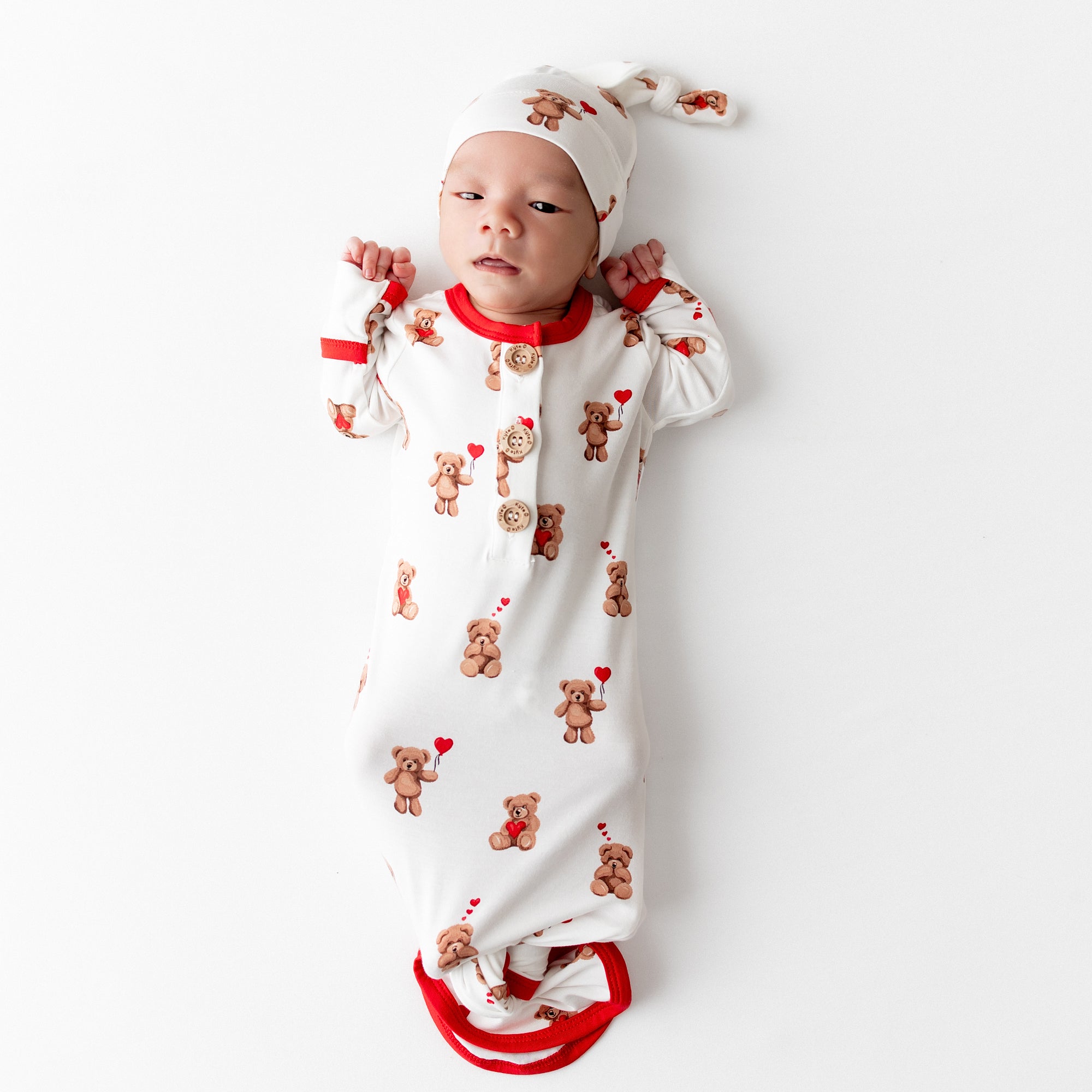 Newborn laying on a white surface wearing the soft Knotted Gown with Hat Set in Bear Hearts