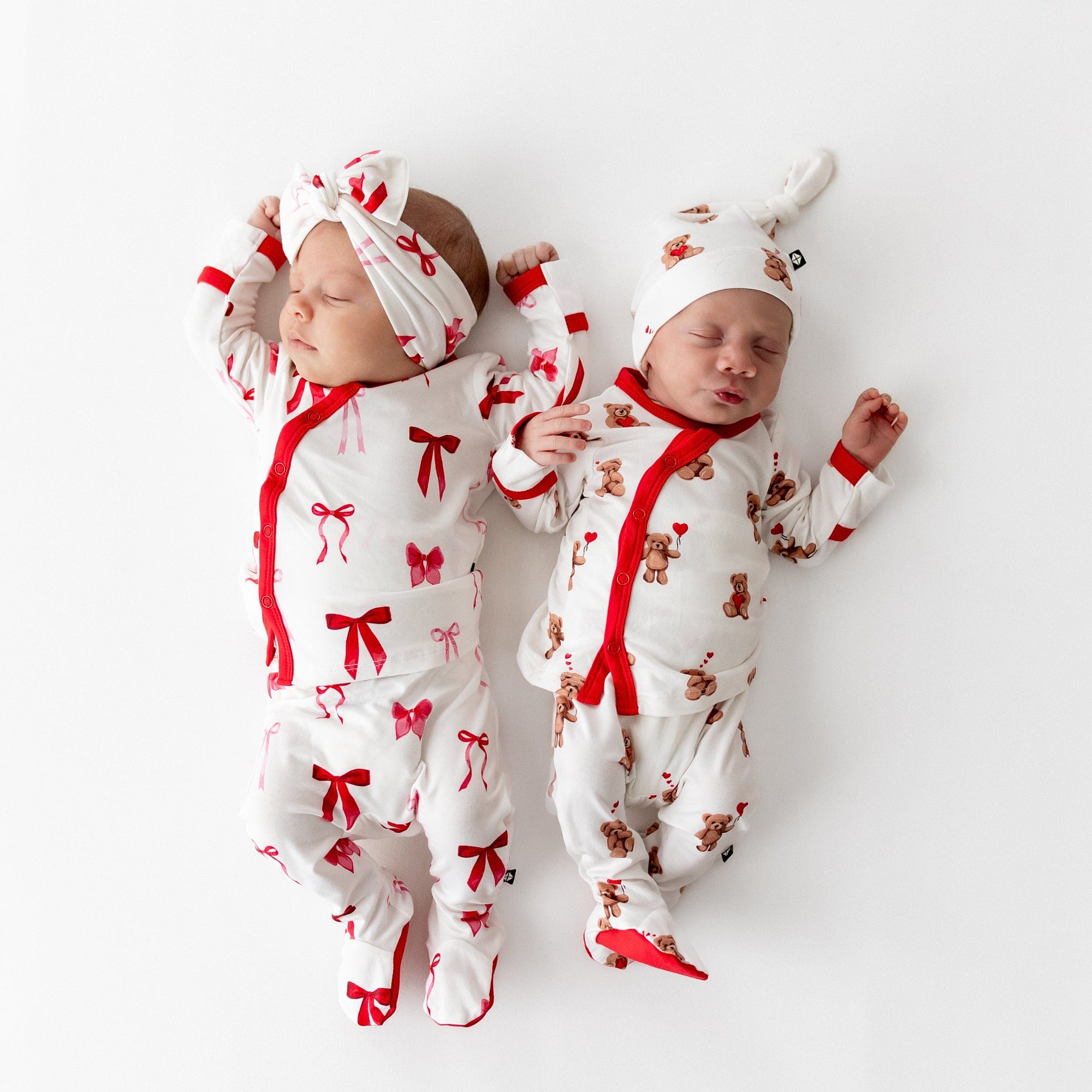 Two sleeping newborns laying side by side wearing the Take Me Home Set with Cap in Bear Hearts and Take me Home Set with Bow in Small Love Bow