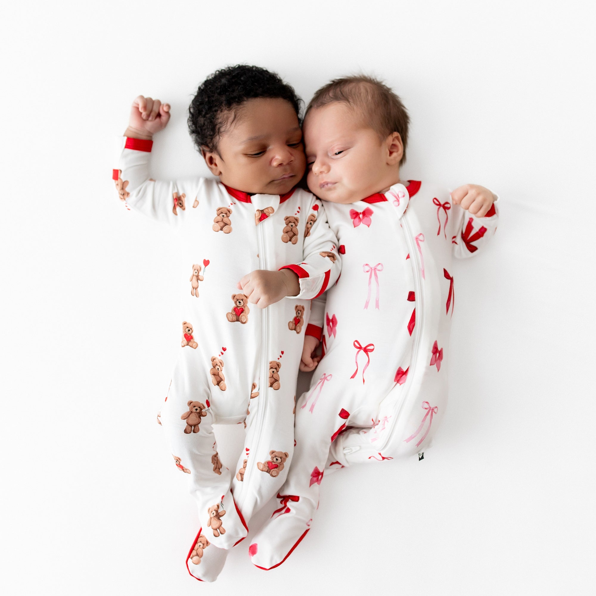 Two newborns laying side by side wearing zippered footies in Bear hearts and Small Love Bow