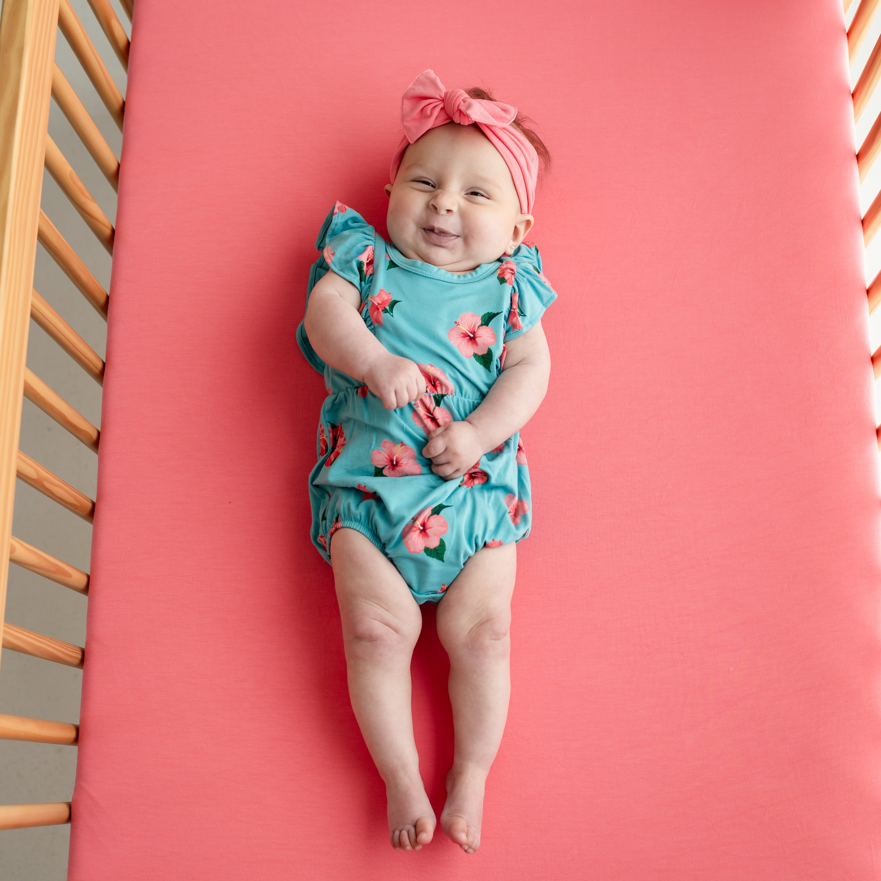 Baby wearing Bubble Romper in Hibiscus and Guava pink bow headband
