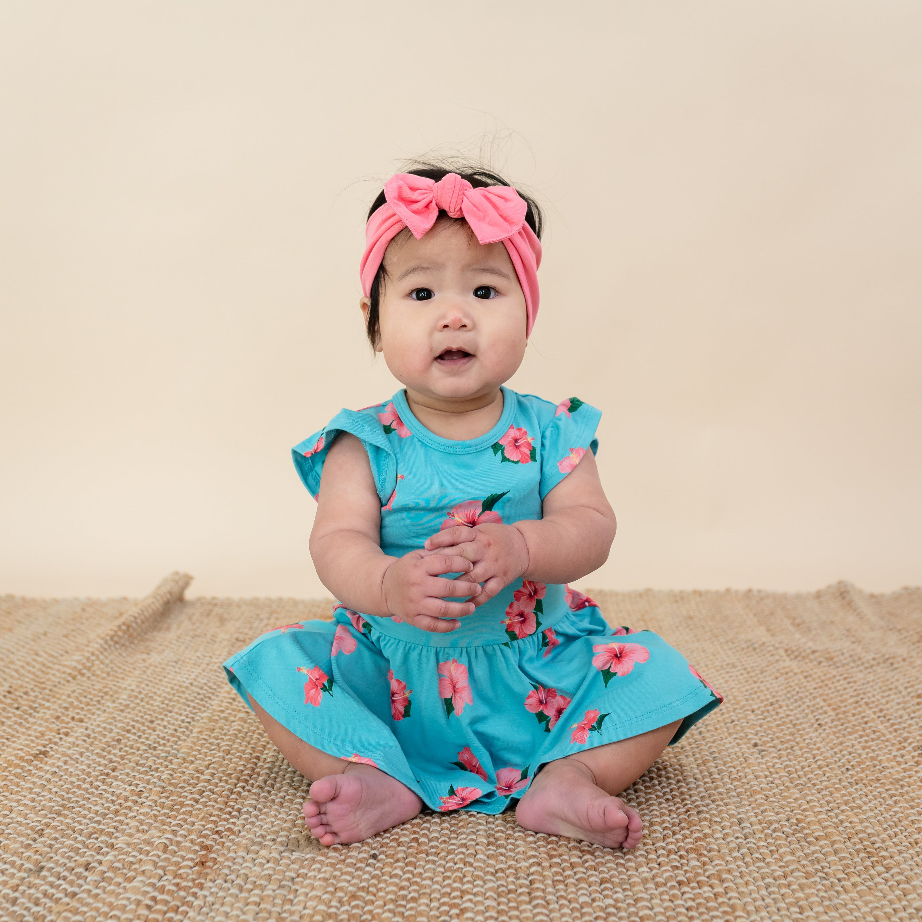 Baby wearing Twirl Bodysuit Dress in Hibiscus with pink bow headband