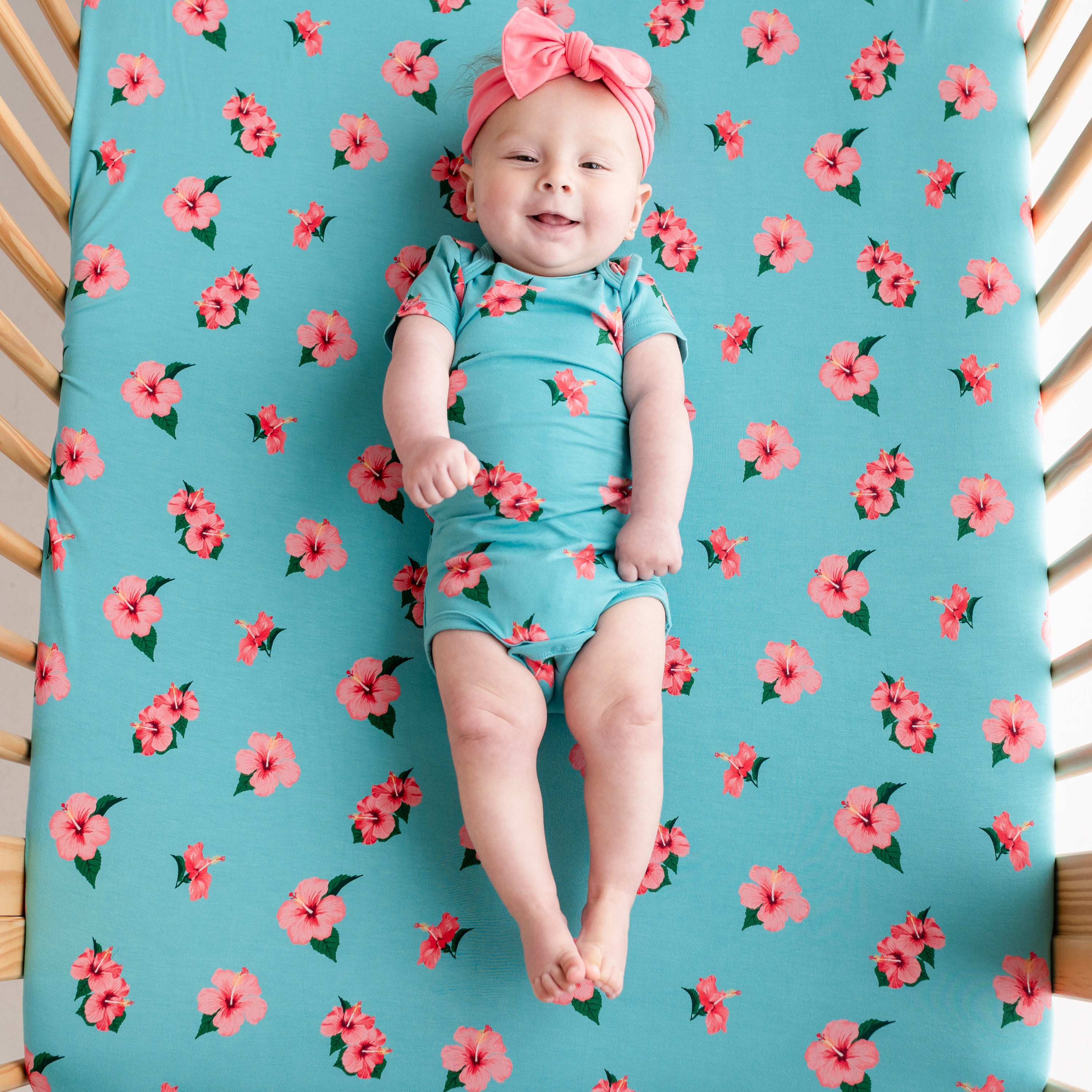 Baby in floral onesie laying in crib with a Hibiscus crib sheet