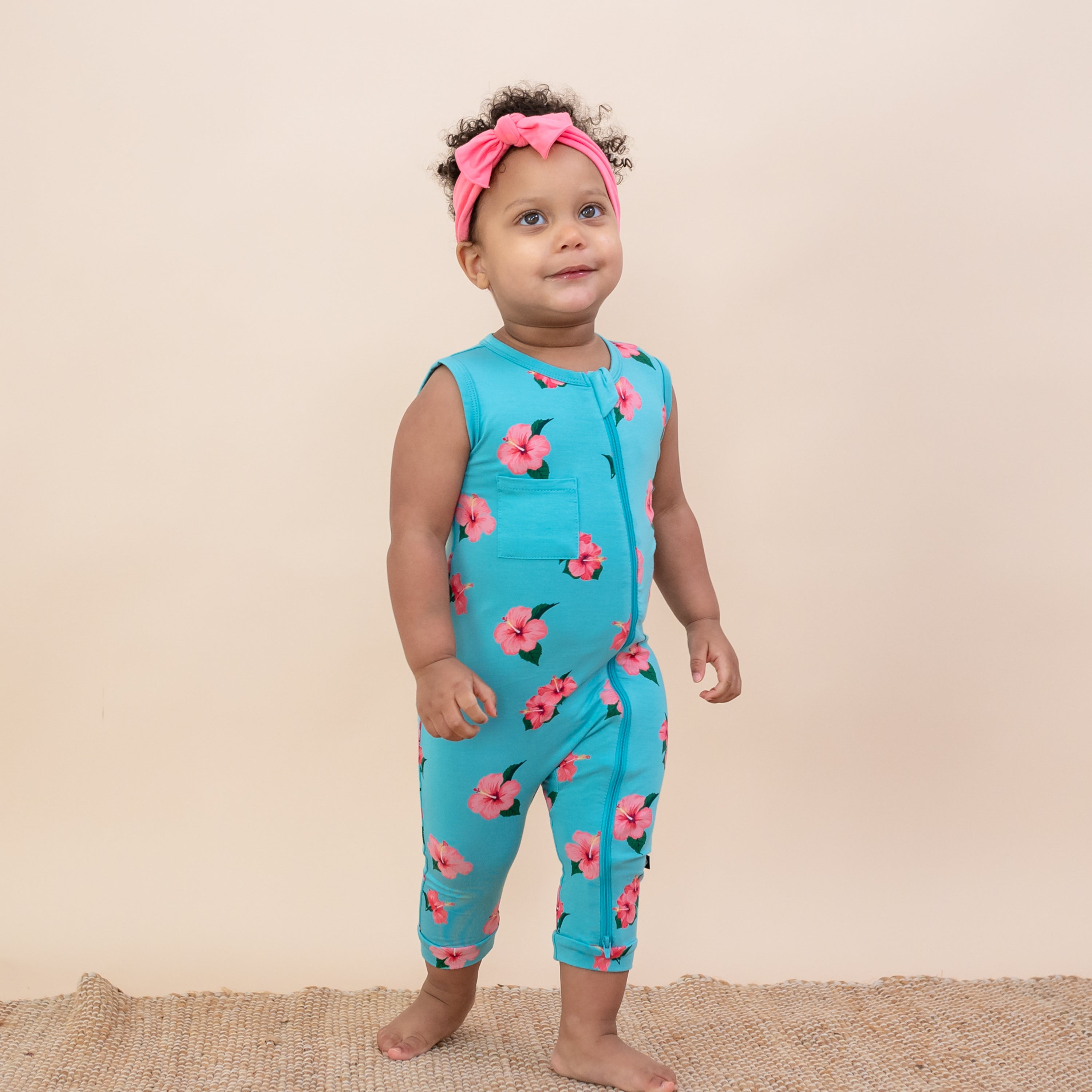 Toddler wearing Kyte Baby Sleeveless Zippered Romper in Hibiscus and Guava Bow