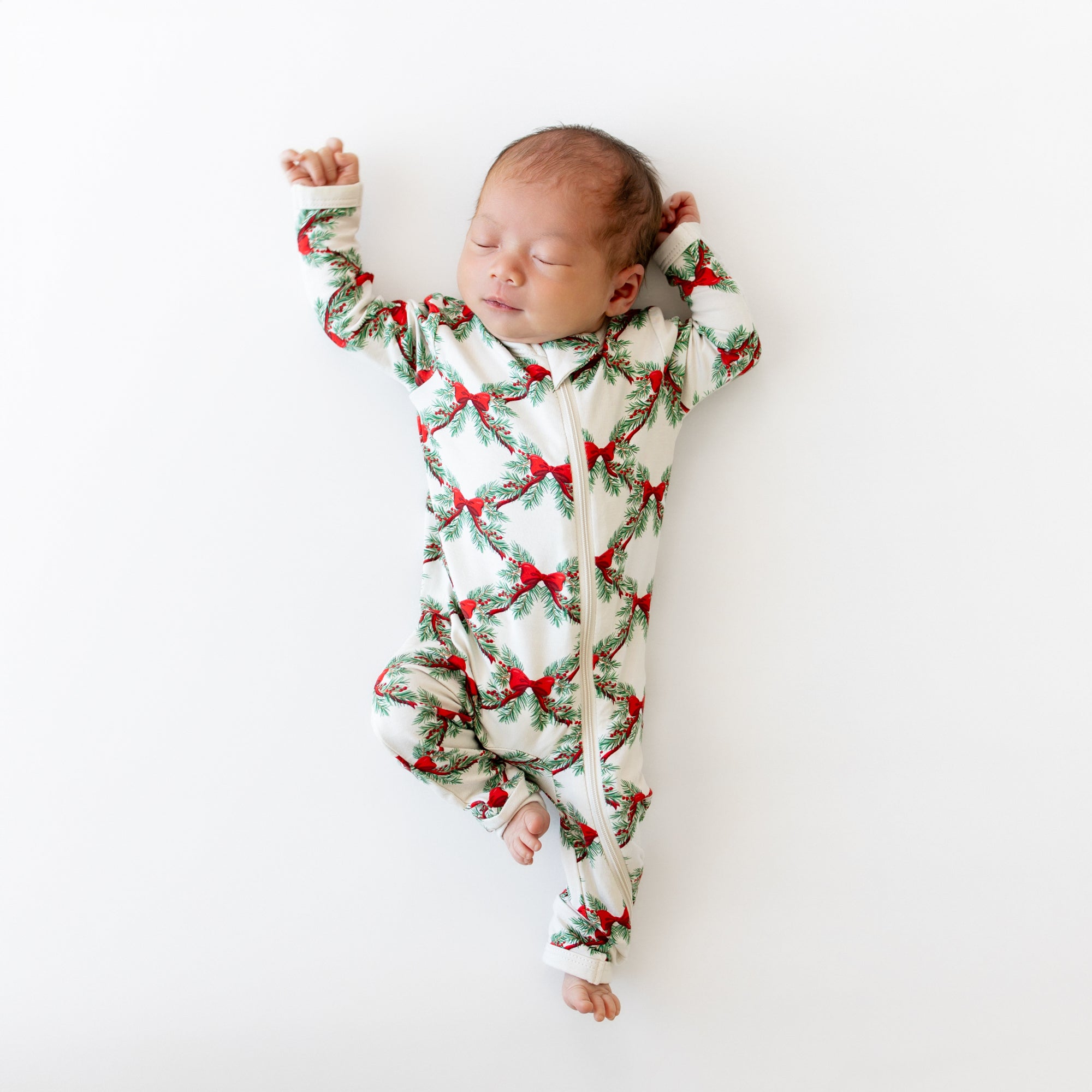 Sleeping newborn laying on a white blanket wearing the Zippered Romper in Holiday Bow