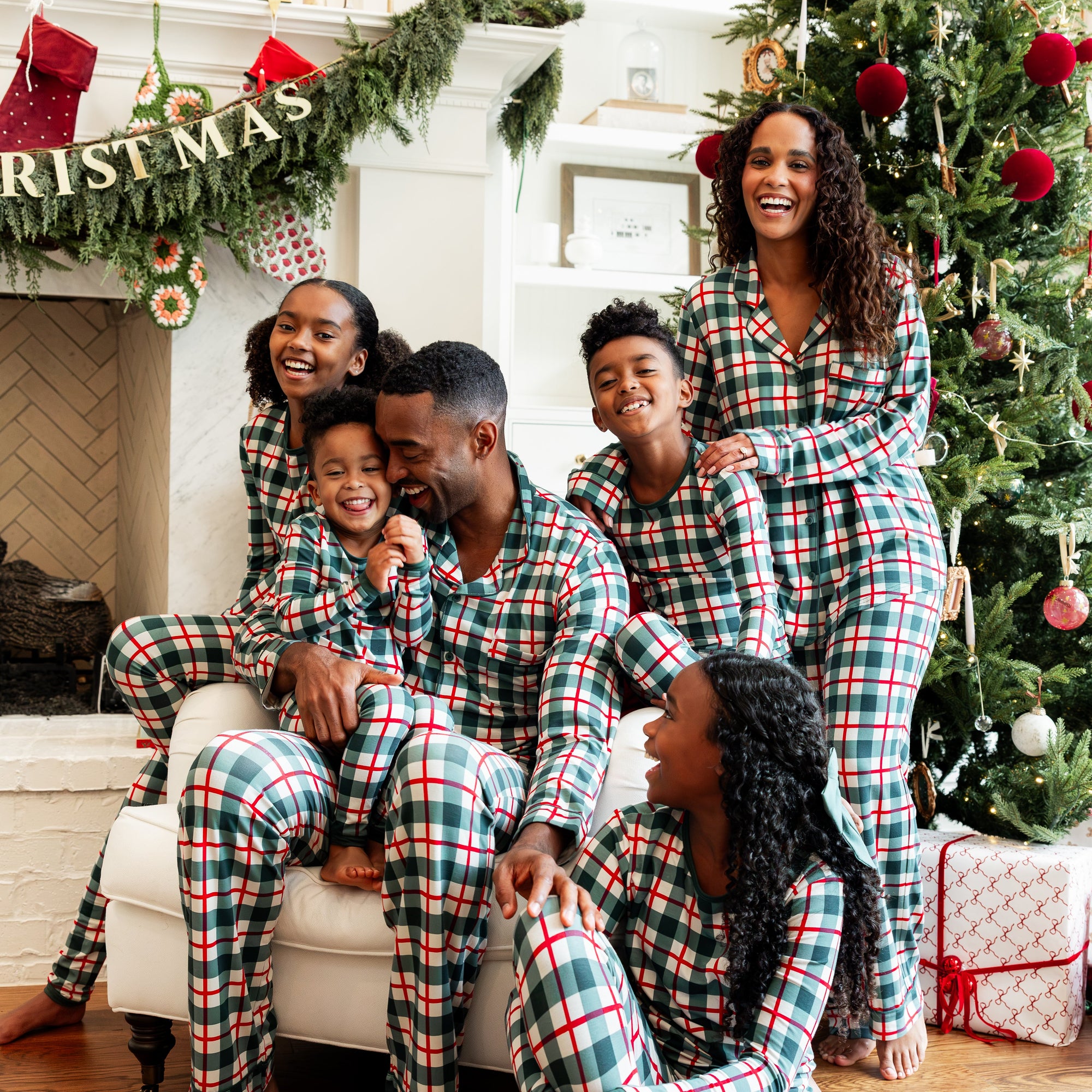 Family of 6 wearing Holiday Plaid matching pajamas with christmas tree behind them