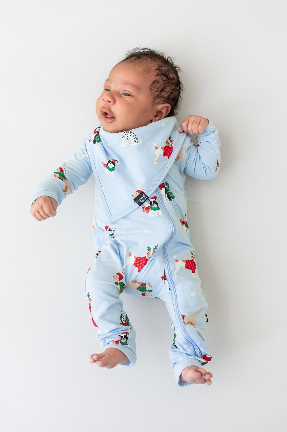Baby wearing Bib in Holiday Pups print over similar print romper on a beige background