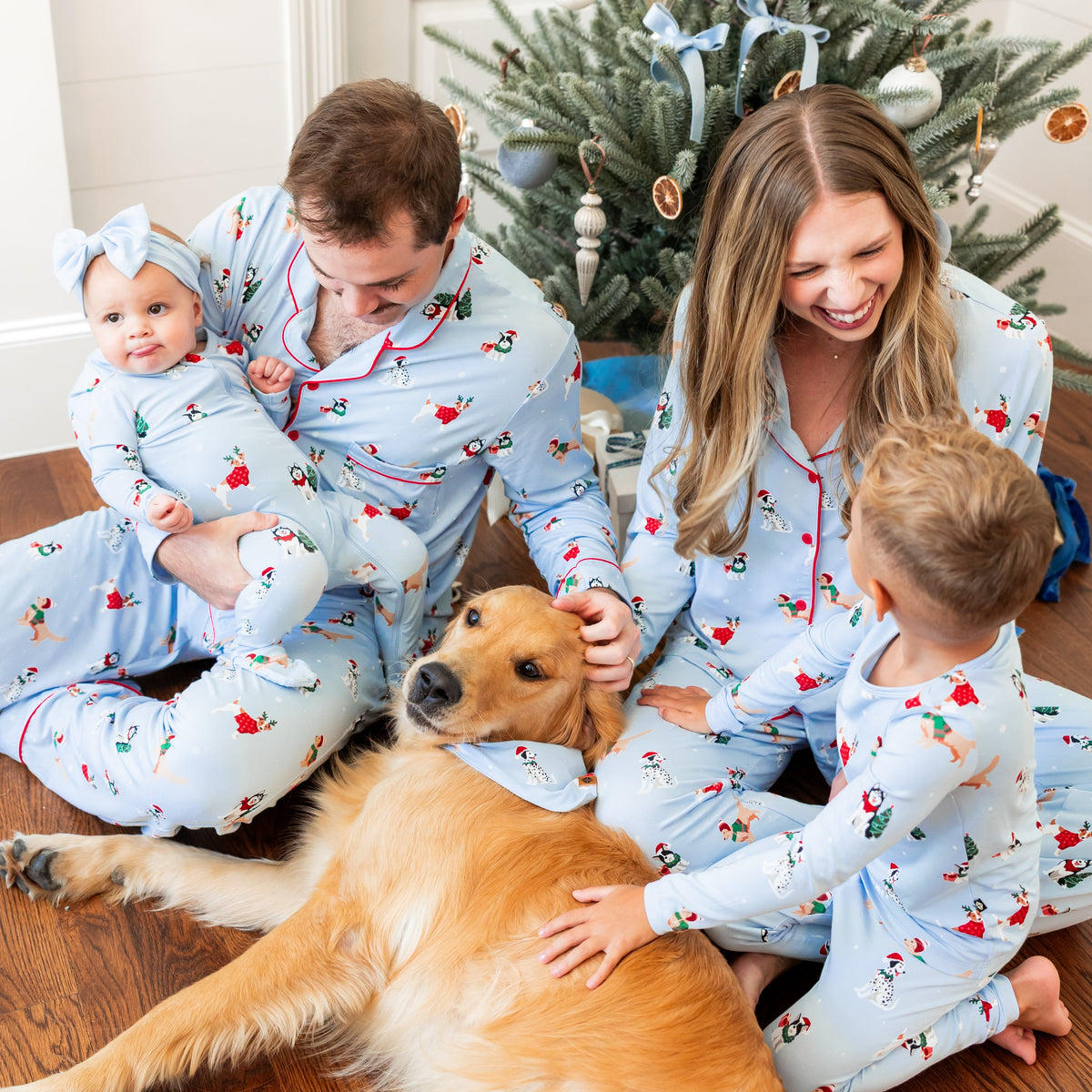 Family of 4 and dog wearing matching blue festive pajamas featuring dogs wearing holiday accessories