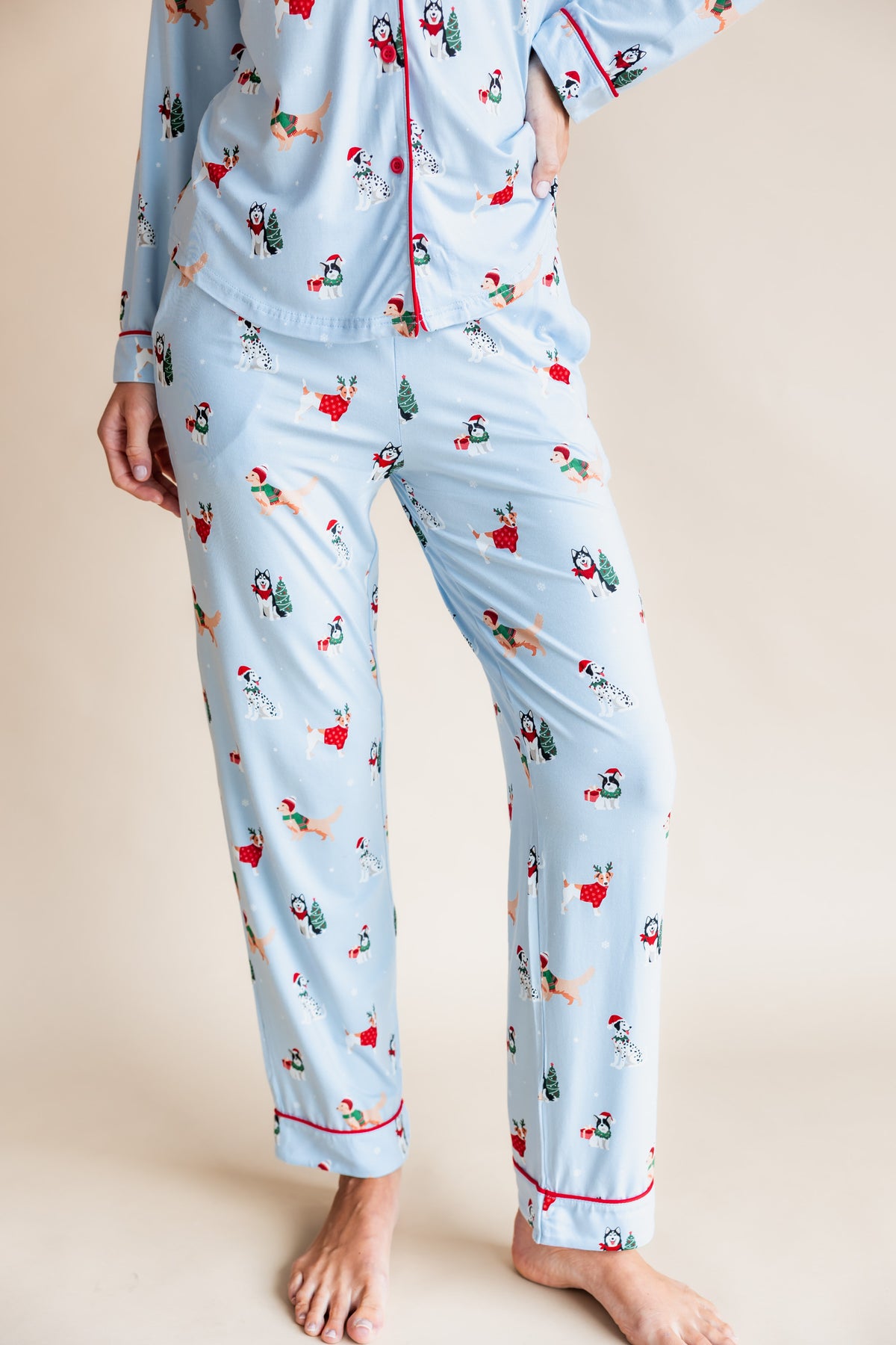 Woman showcasing the front side of Long-Sleeved Women's Pajama Set in Holiday Pups print on a beige background
