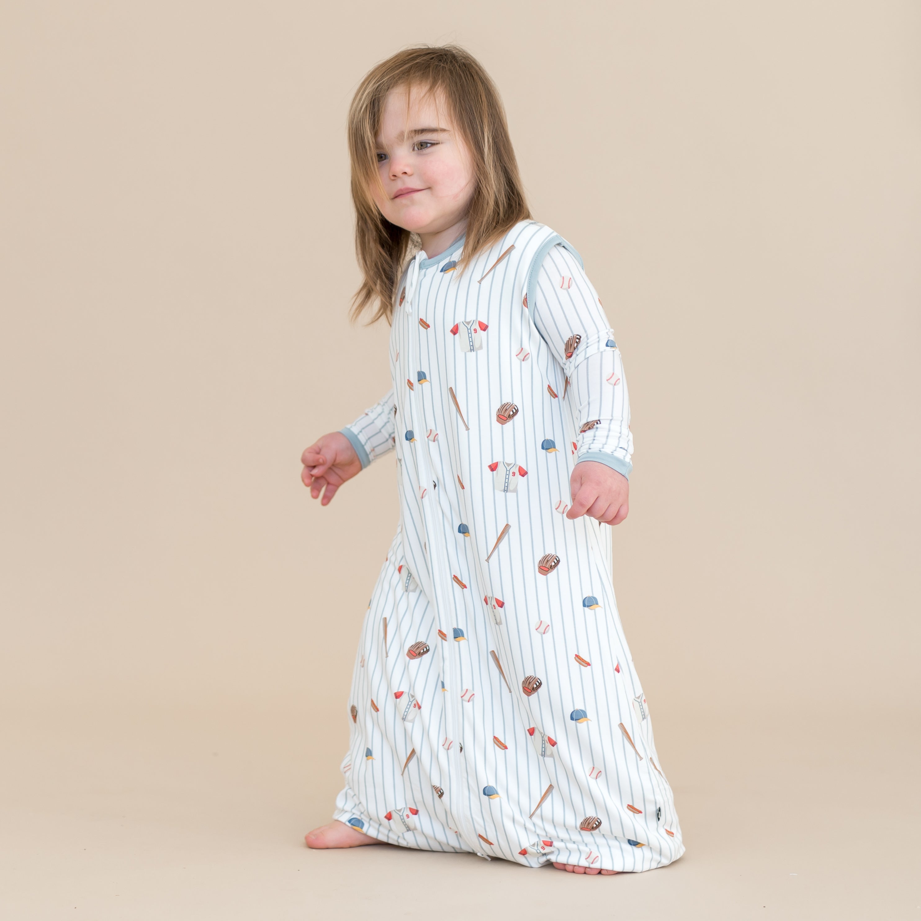 Young child walking wearing the Sleep Bag Walker in Home Run 0.5 with matching long sleeve pajamas on underneath