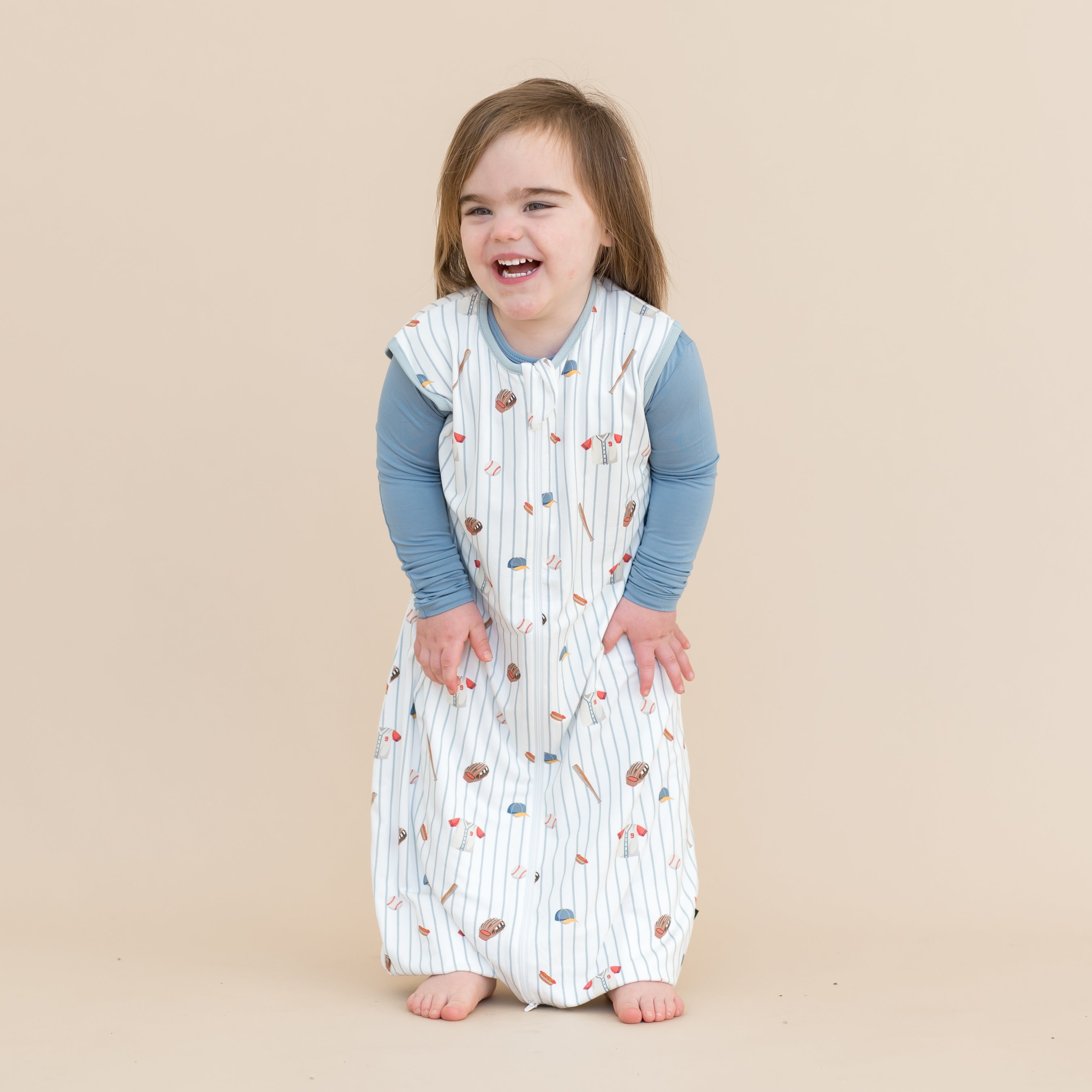 Smiling young child wearing the Sleep Bag Walker in Home Run 0.5 with Slate long sleeve pajamas on underneath