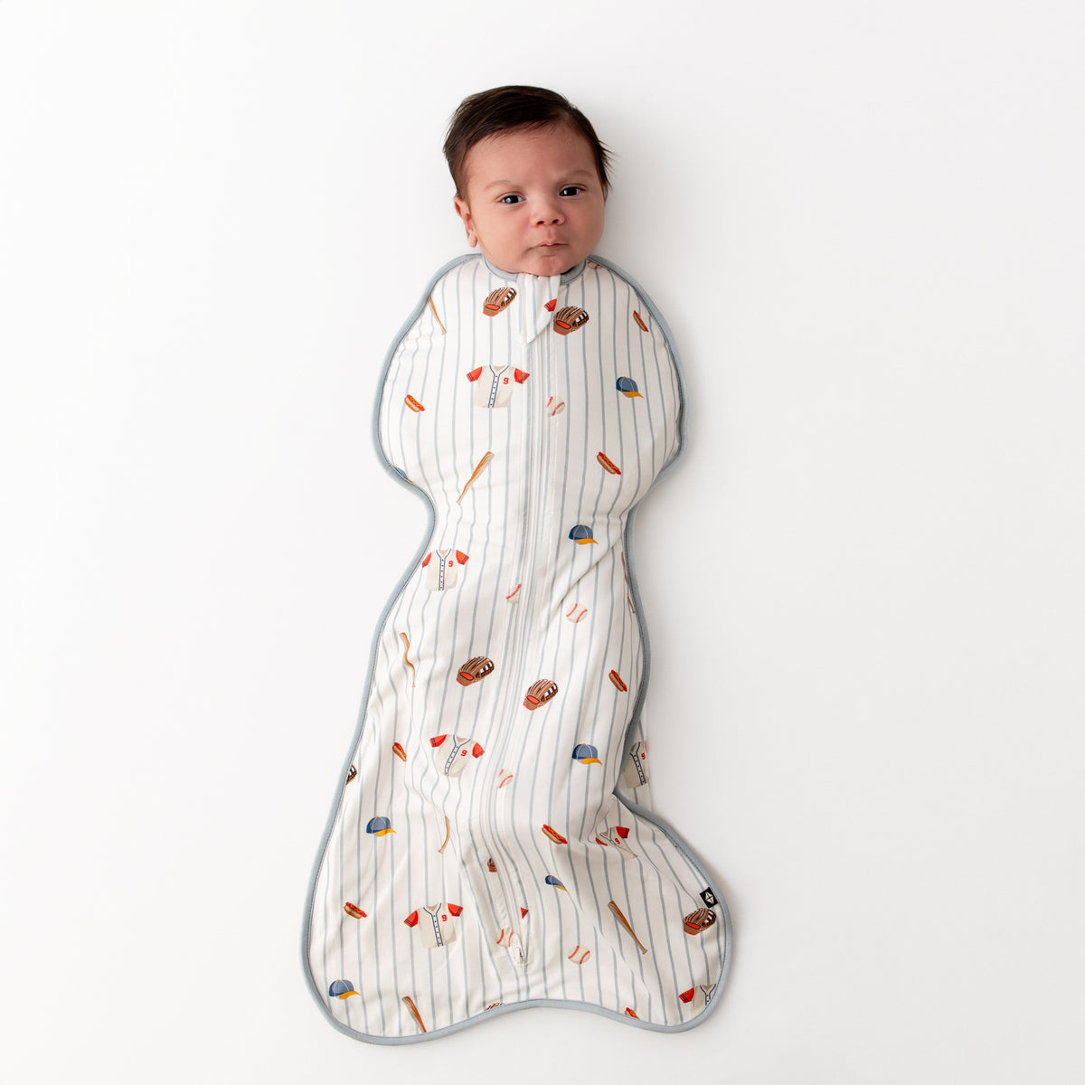 Newborn laying on a white surface wearing the Swaddle Bag in Home Run 0.5