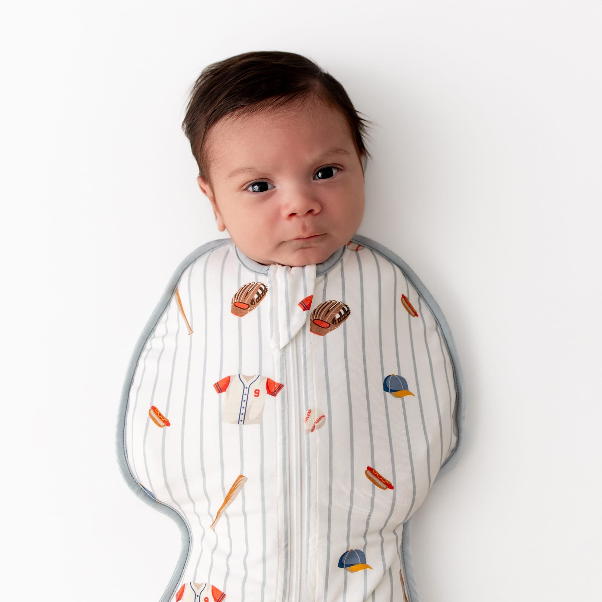 Close up of newborn wearing the Swaddle Bag in Home Run 0.5 laying on a white surface