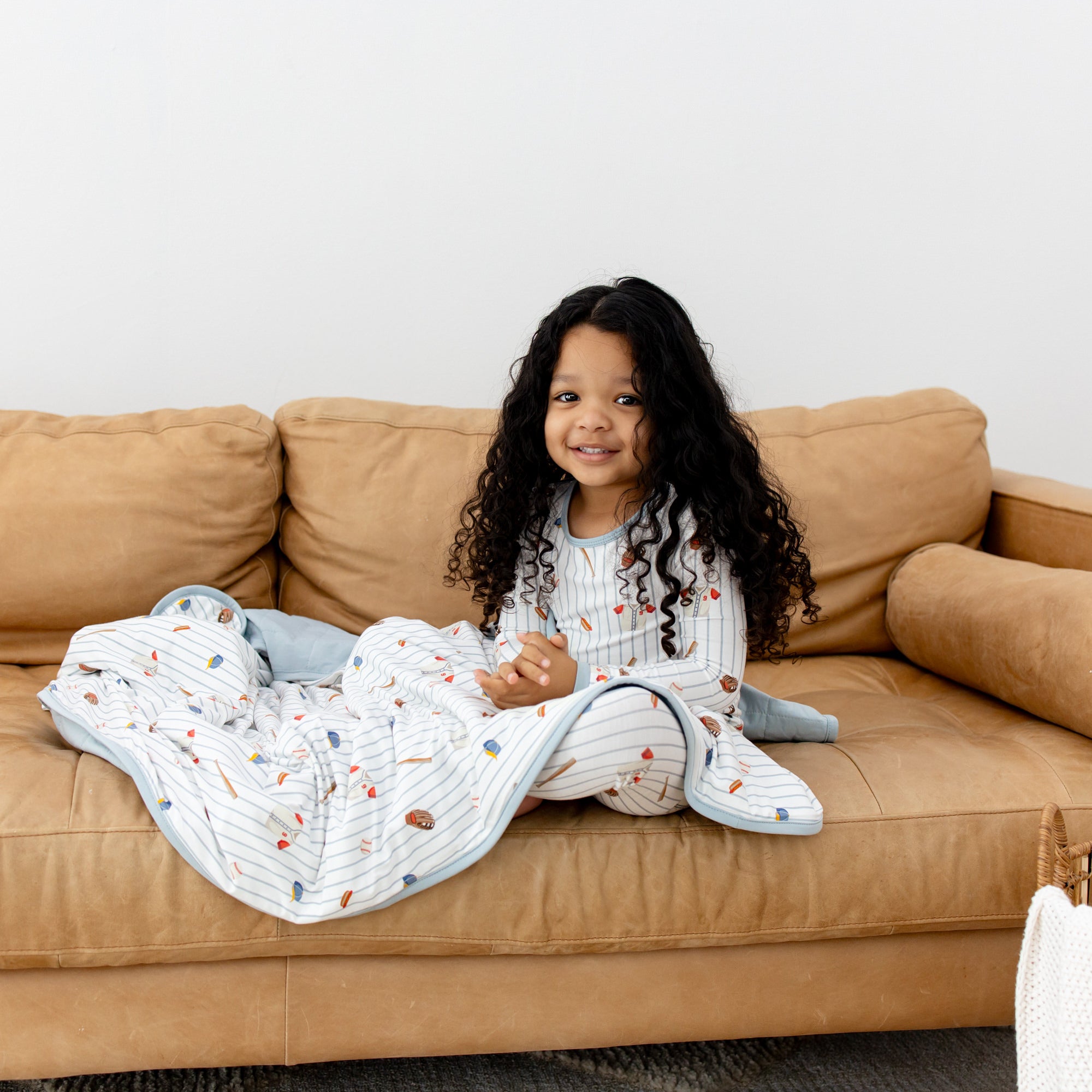 Young girls sitting on a brown couch wearing the Toddler Blanket in Home Run 1.0 with matching long sleeve pajamas