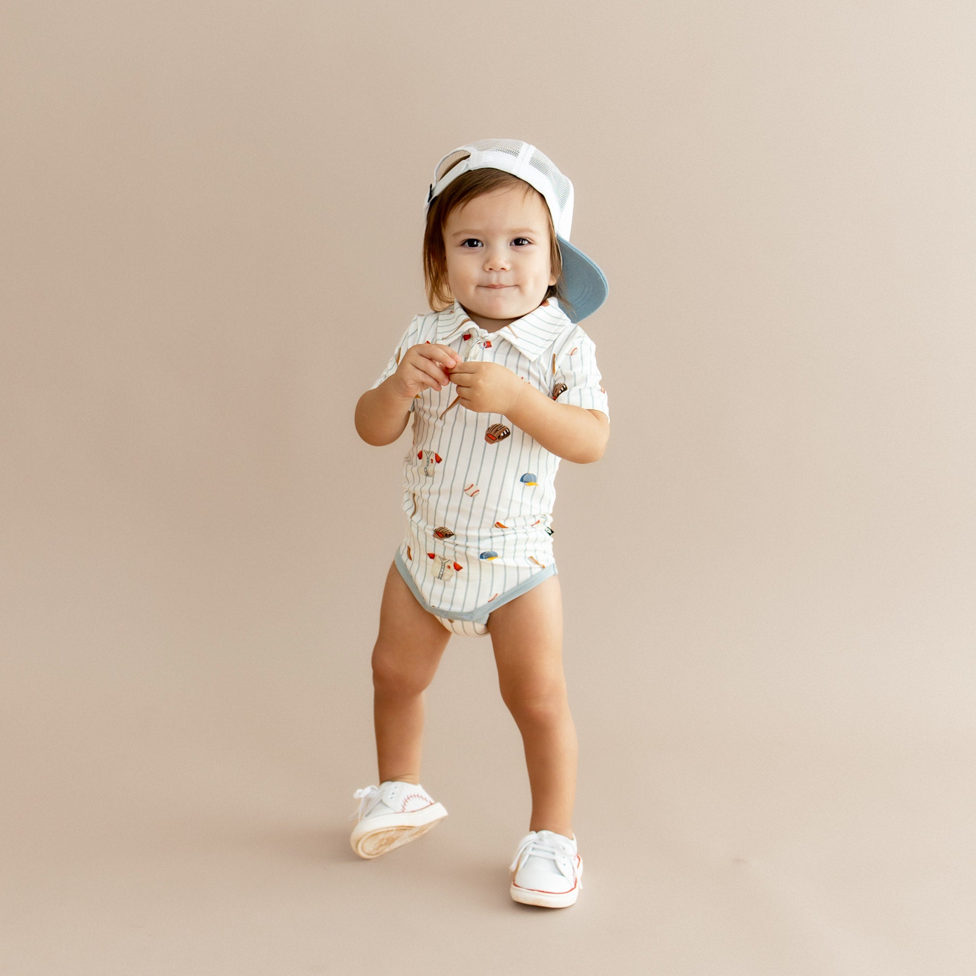 Young boy wearing the Polo Bodysuit Home Run paired with a baseball cap and white sneakers