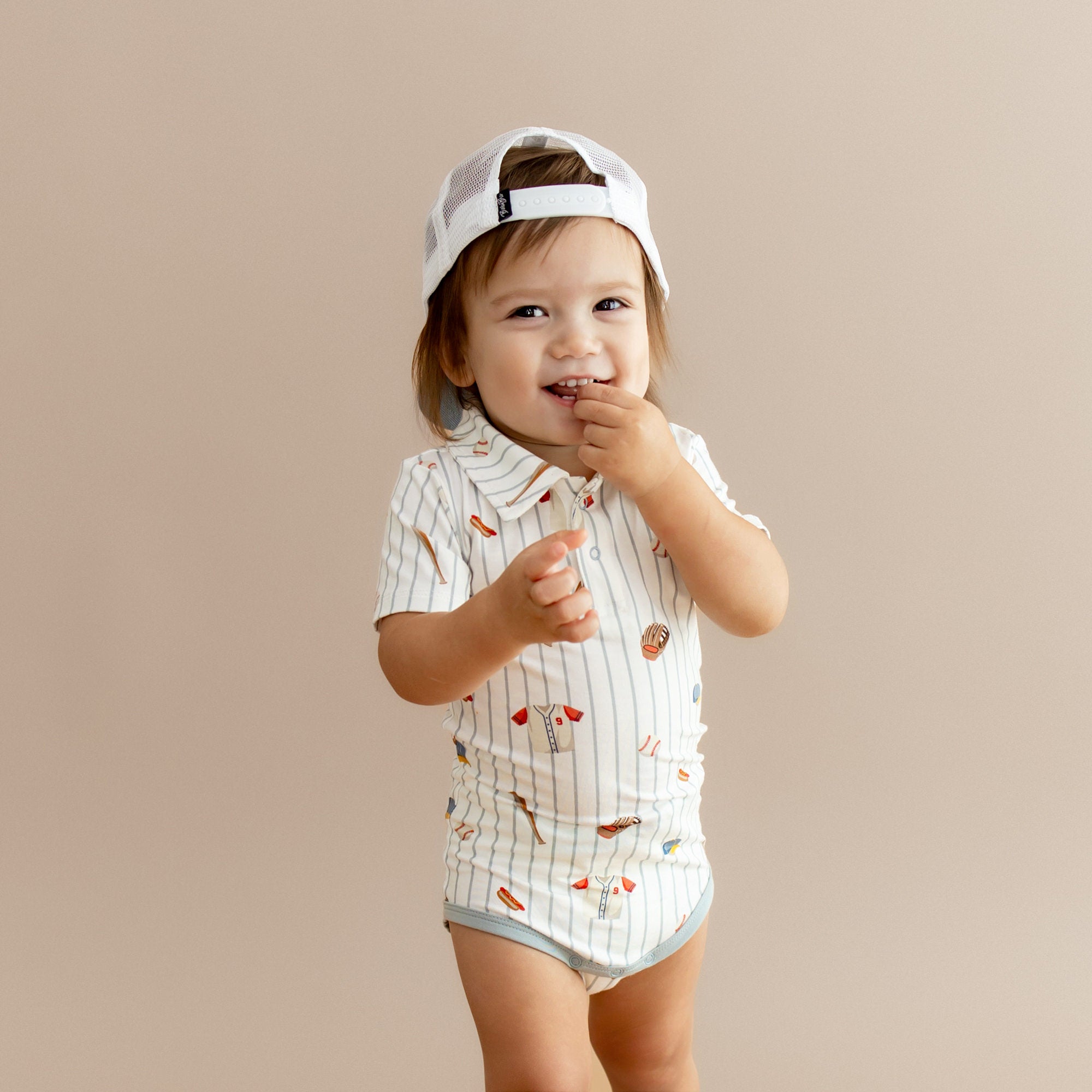 Close up of young boy wearing the Polo Bodysuit Home Run with a backwards baseball cap