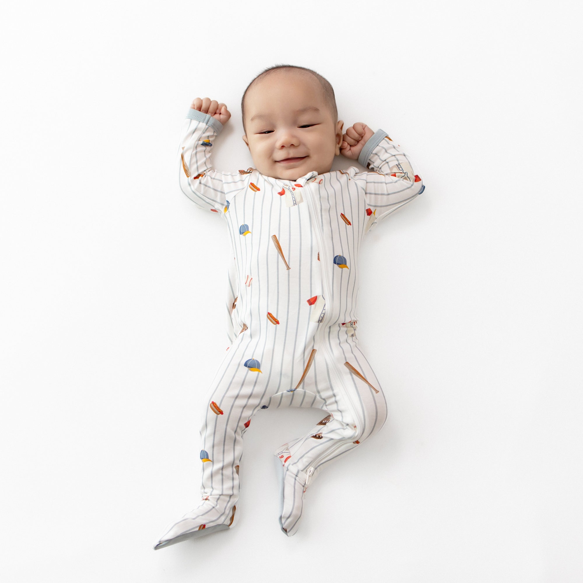 Infant laying on a white surface wearing the Zippered Footie in Home Run