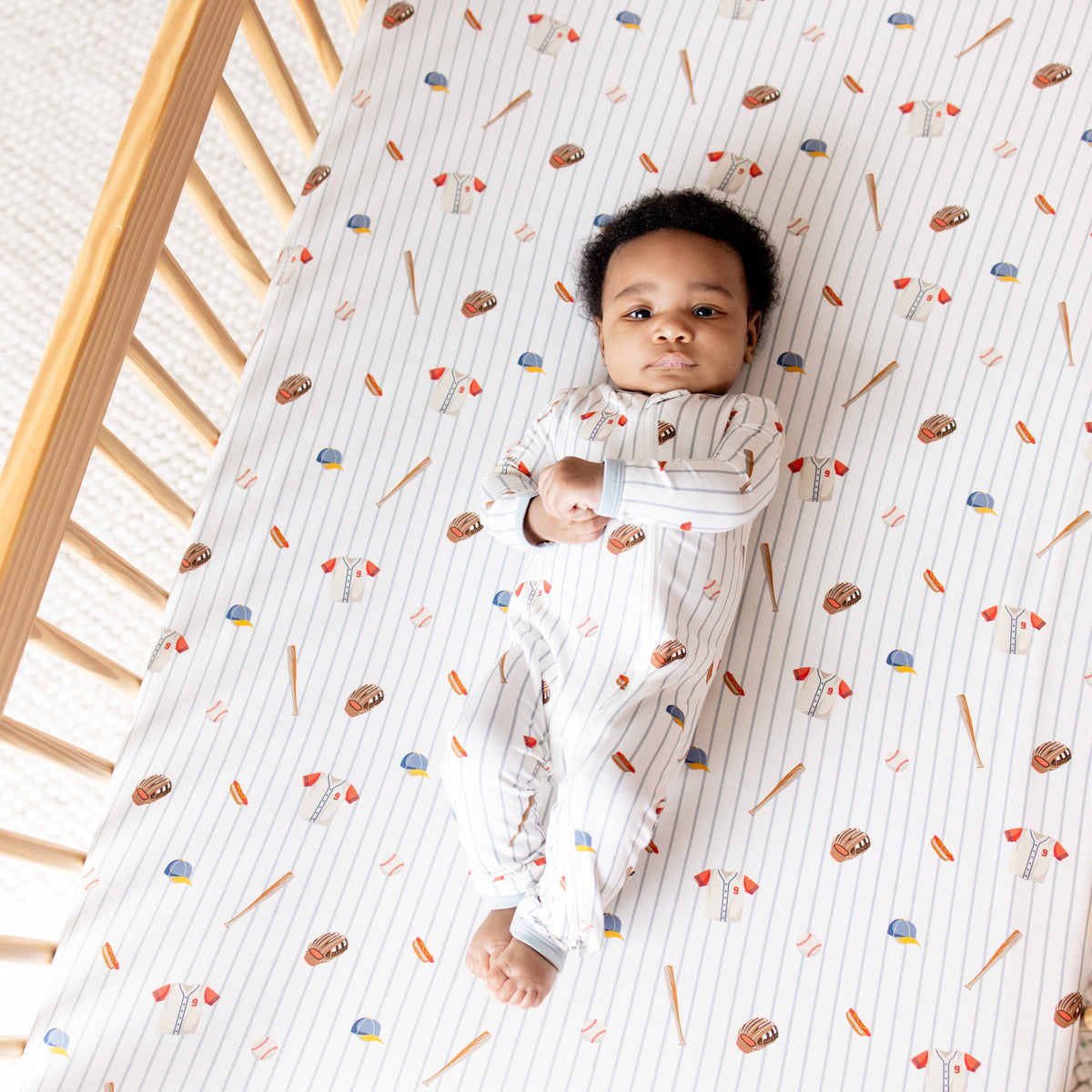 Infant laying in a crib on a Crib Sheet in Home Run wearing a matching zippered romper