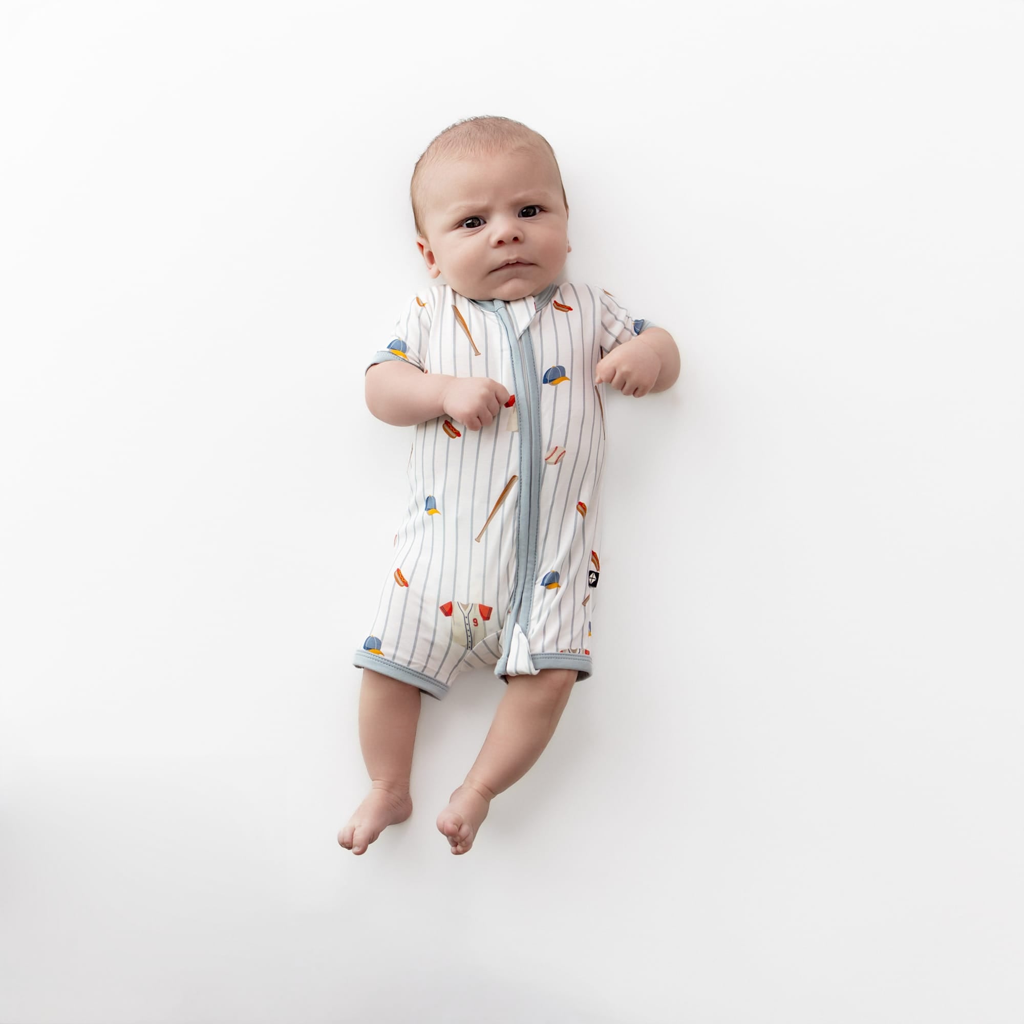 Infant laying on a white surface wearing the Zipper Shortall Romper in Home Run