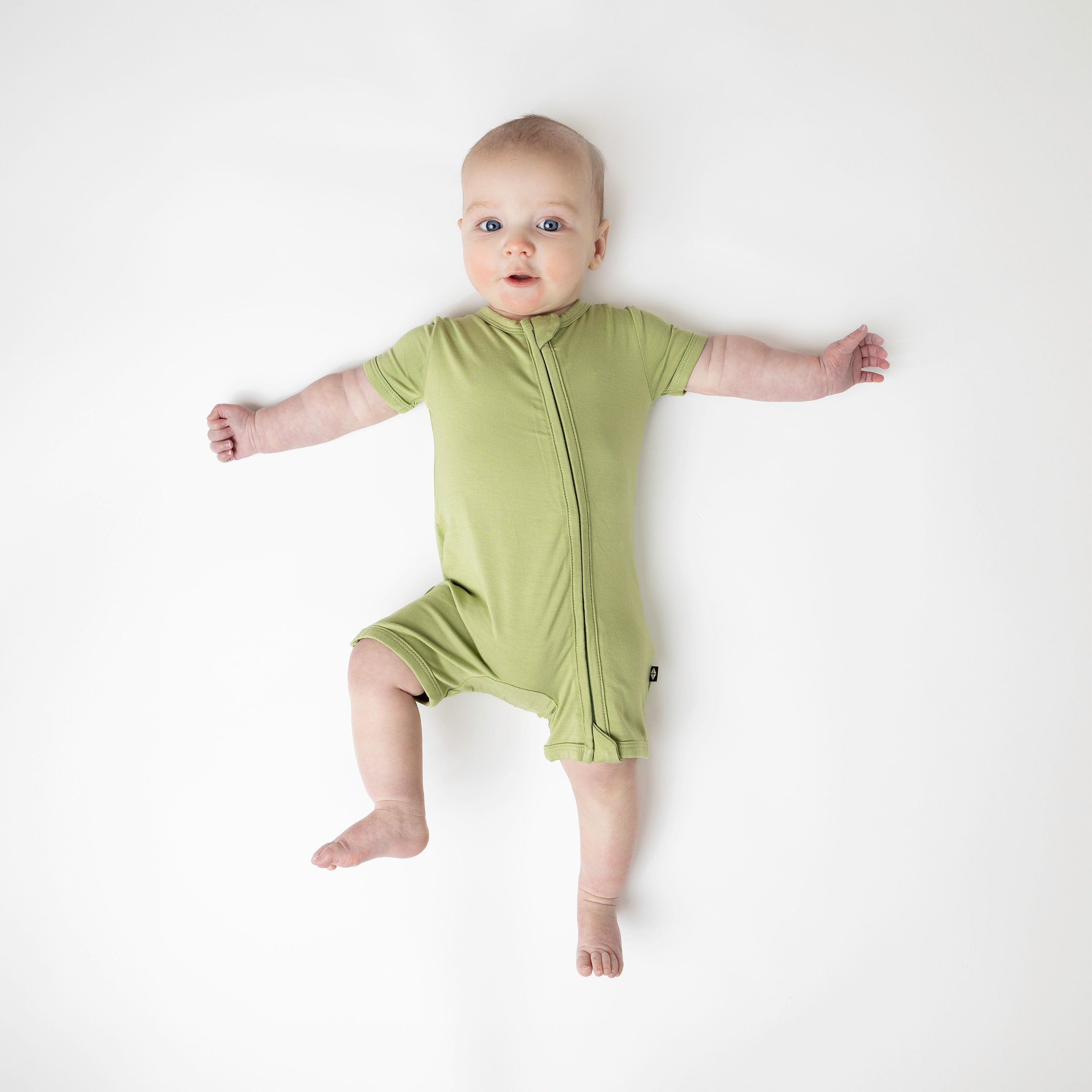 Infant wearing Kyte Baby Zippered Shortall Romper with dual zipper in Honu green
