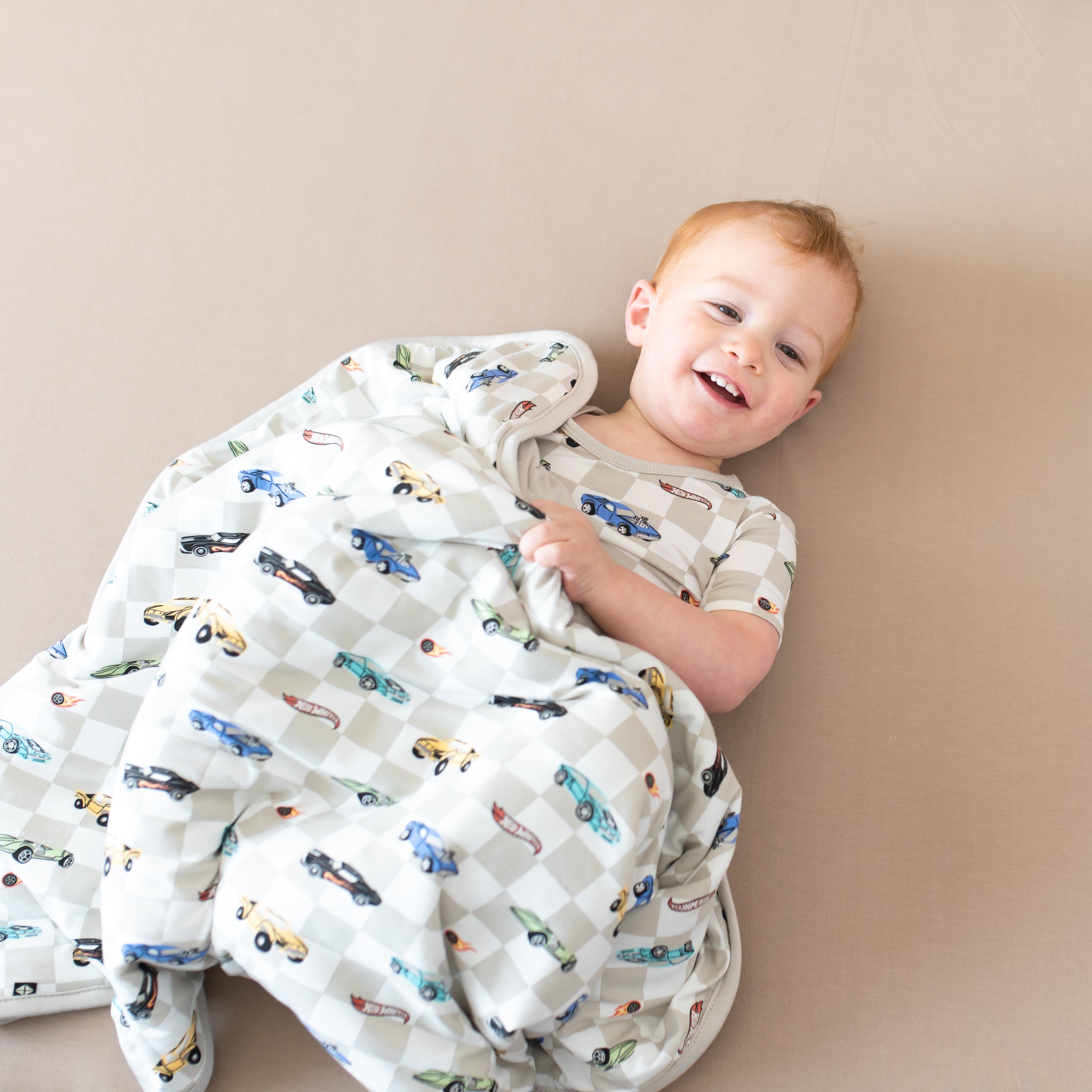 Smiling toddler laying down underneath the Baby Blanket in Fast and Fierce 1.0 wearing matching short sleeve pajamas