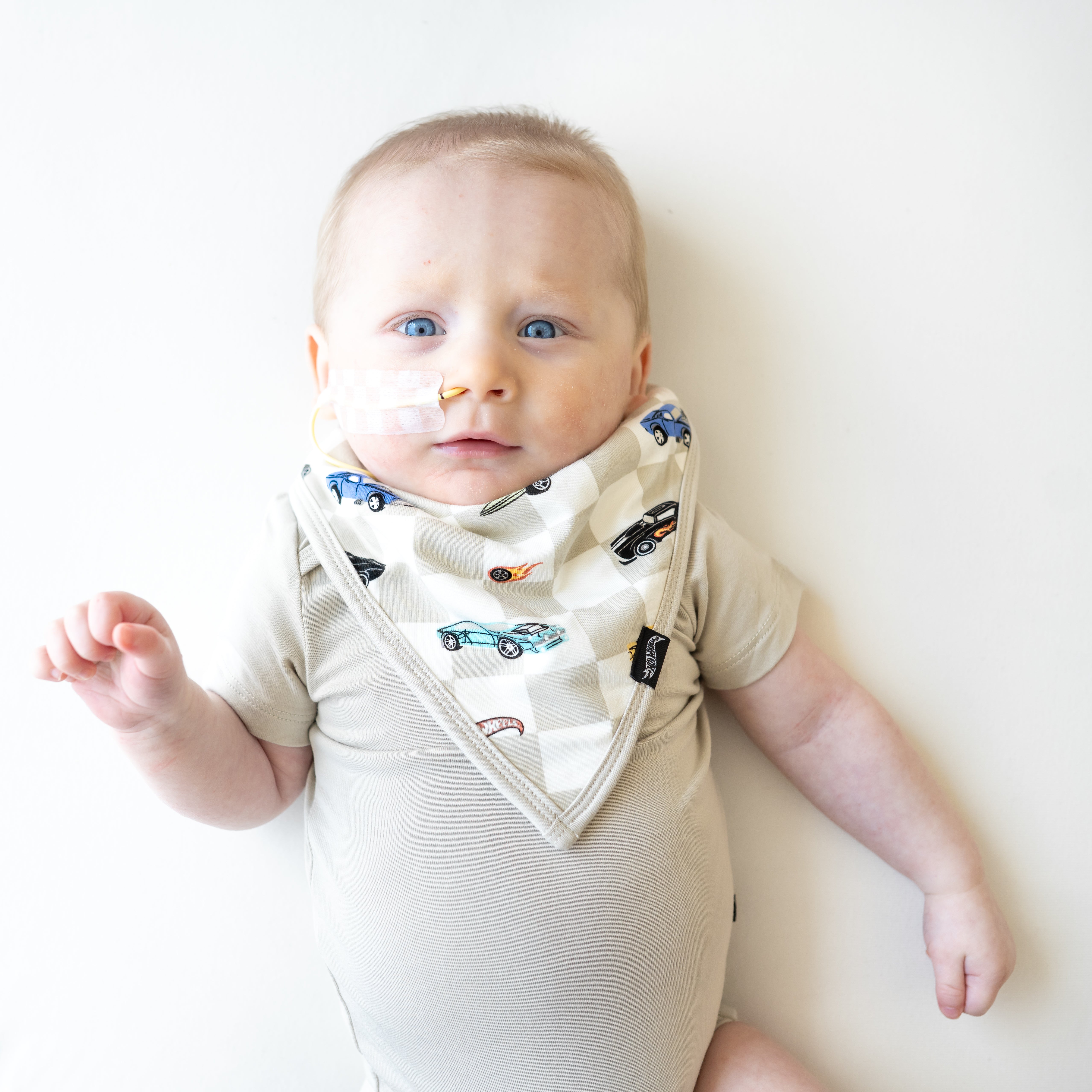 Infant laying down with one hand in the air wearing the Bib in Fast and Fierce paired with an Oat Short Sleeve Bodysuit