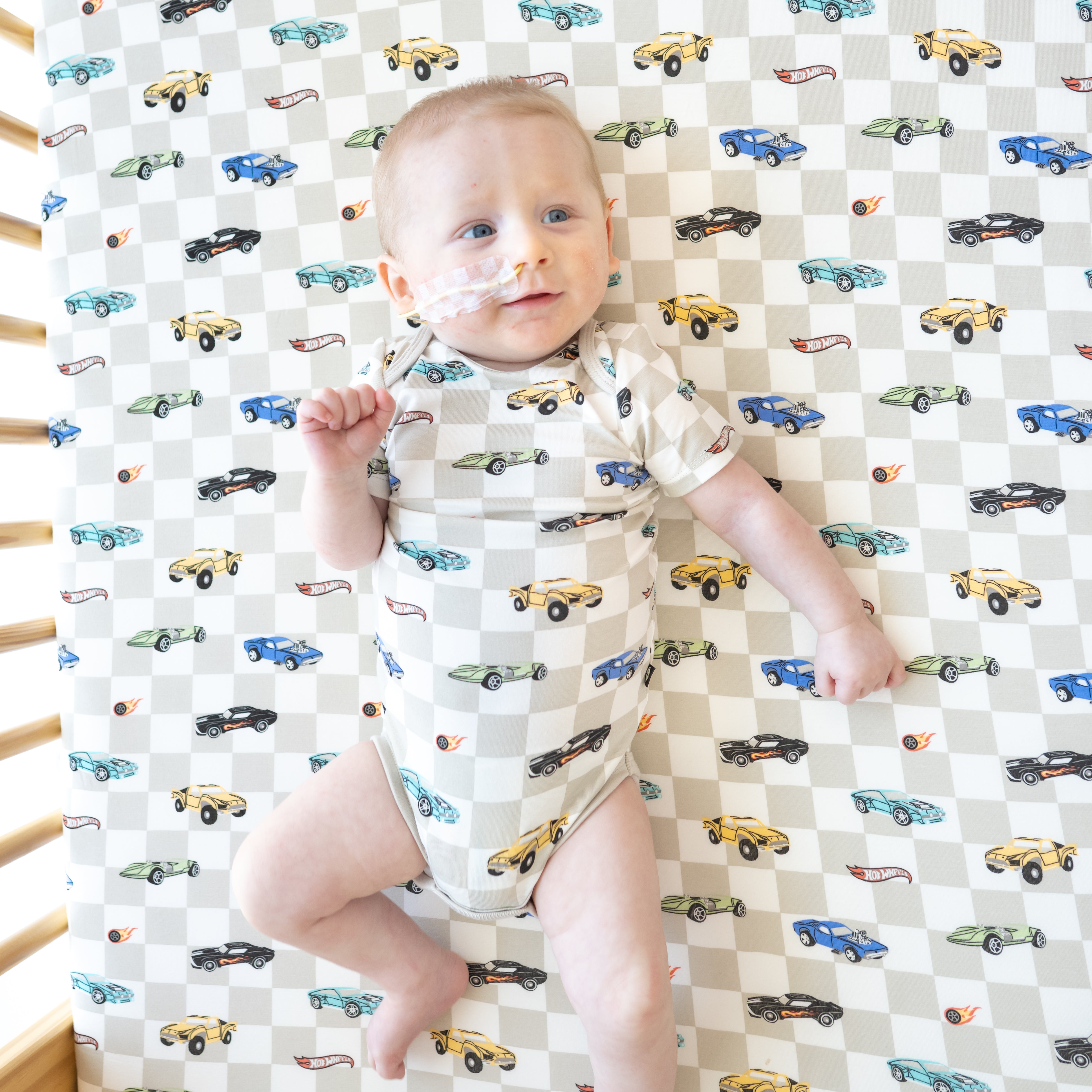 Infant wearing the Bodysuit in Fast and Fierce laying in a crib on a matching Crib Sheet in Fast and Fierce