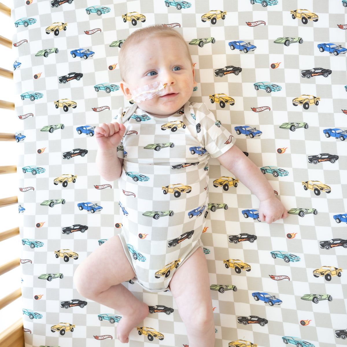 Infant wearing the Bodysuit in Fast and Fierce laying in a crib on a matching Crib Sheet in Fast and Fierce
