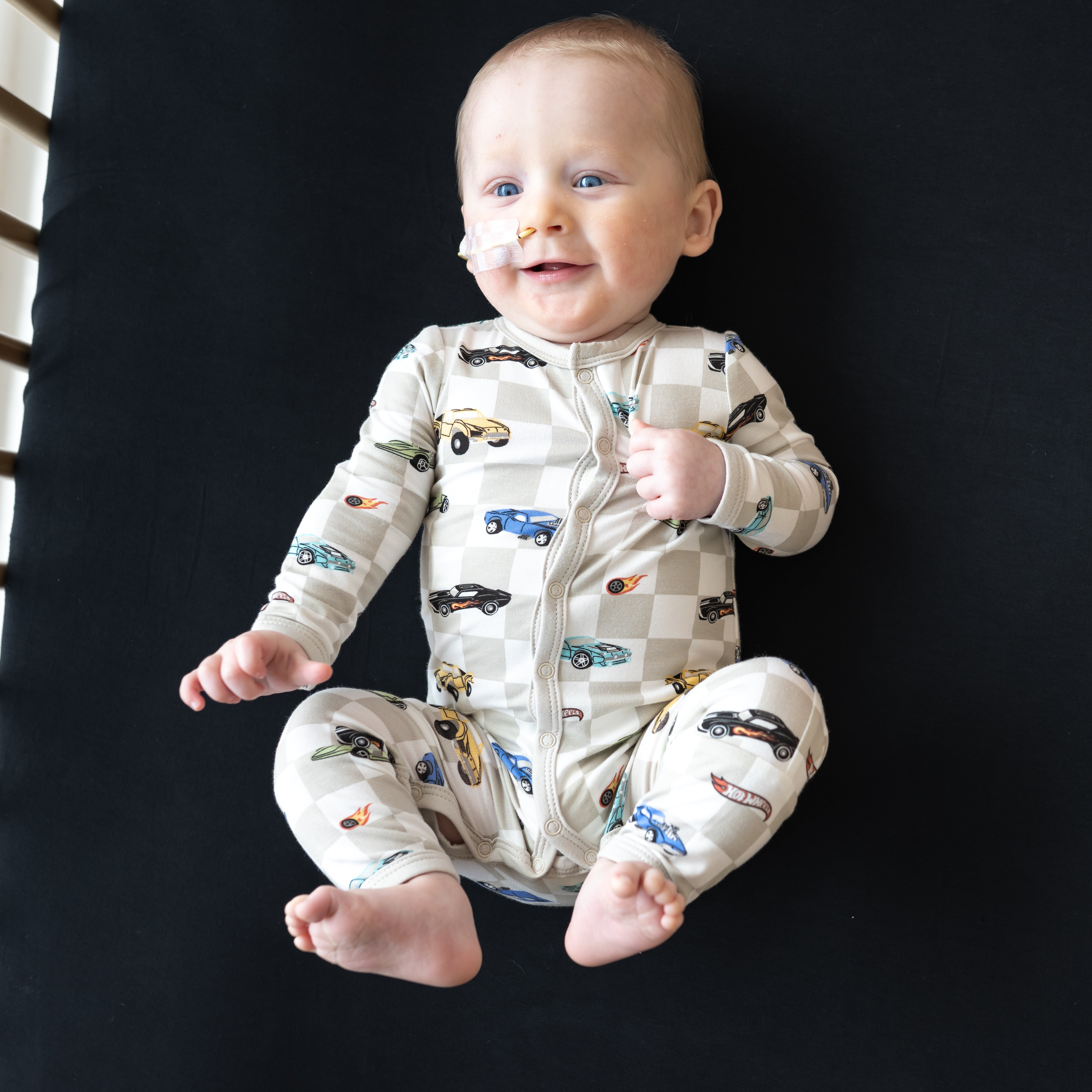 Smiling infant with feet in the air laying in a crib on a Midnight Crib Sheet wearing the Romper in Fast and Fierce