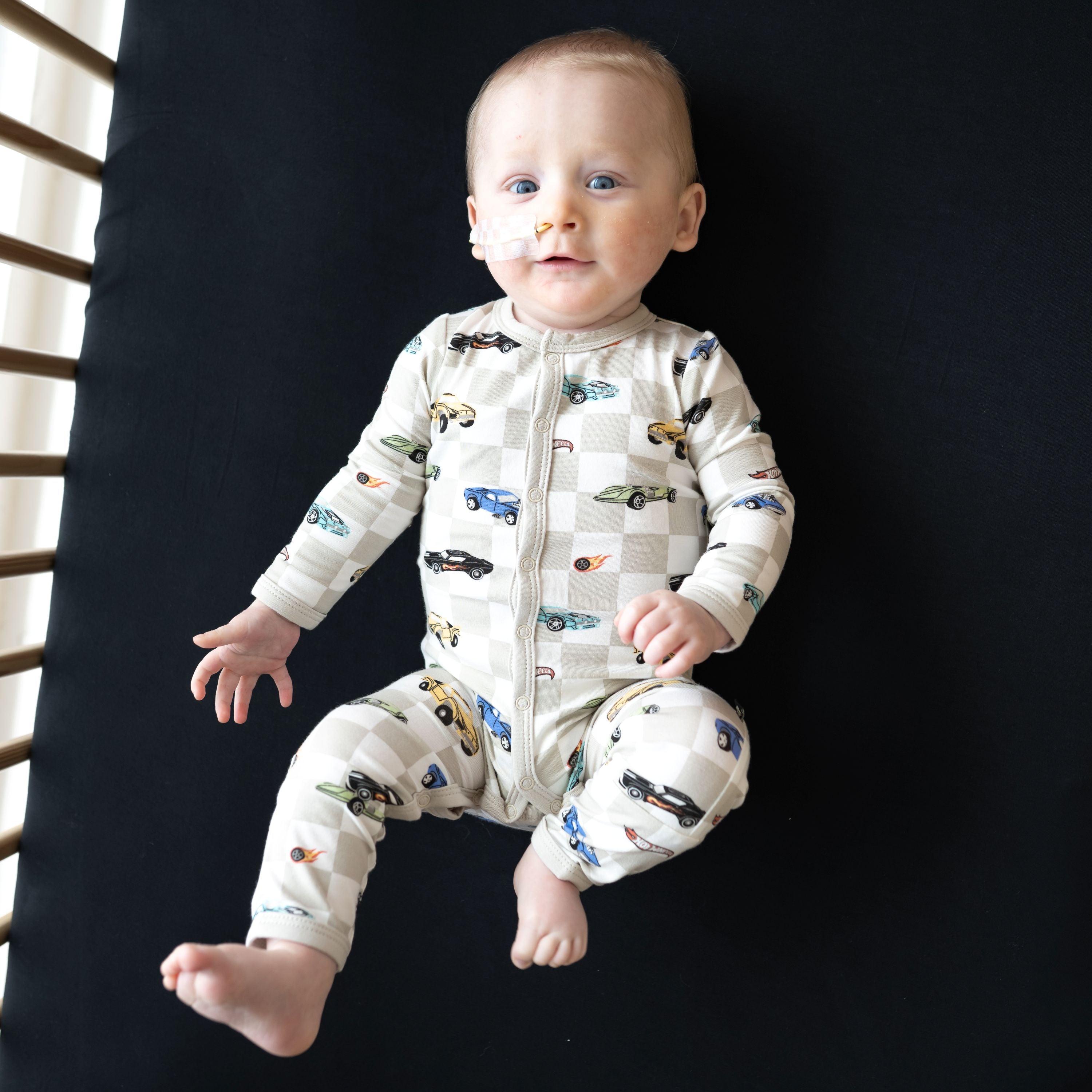 Infant laying in a crib on a Midnight Crib sheet wearing the Romper in Fast and Fierce