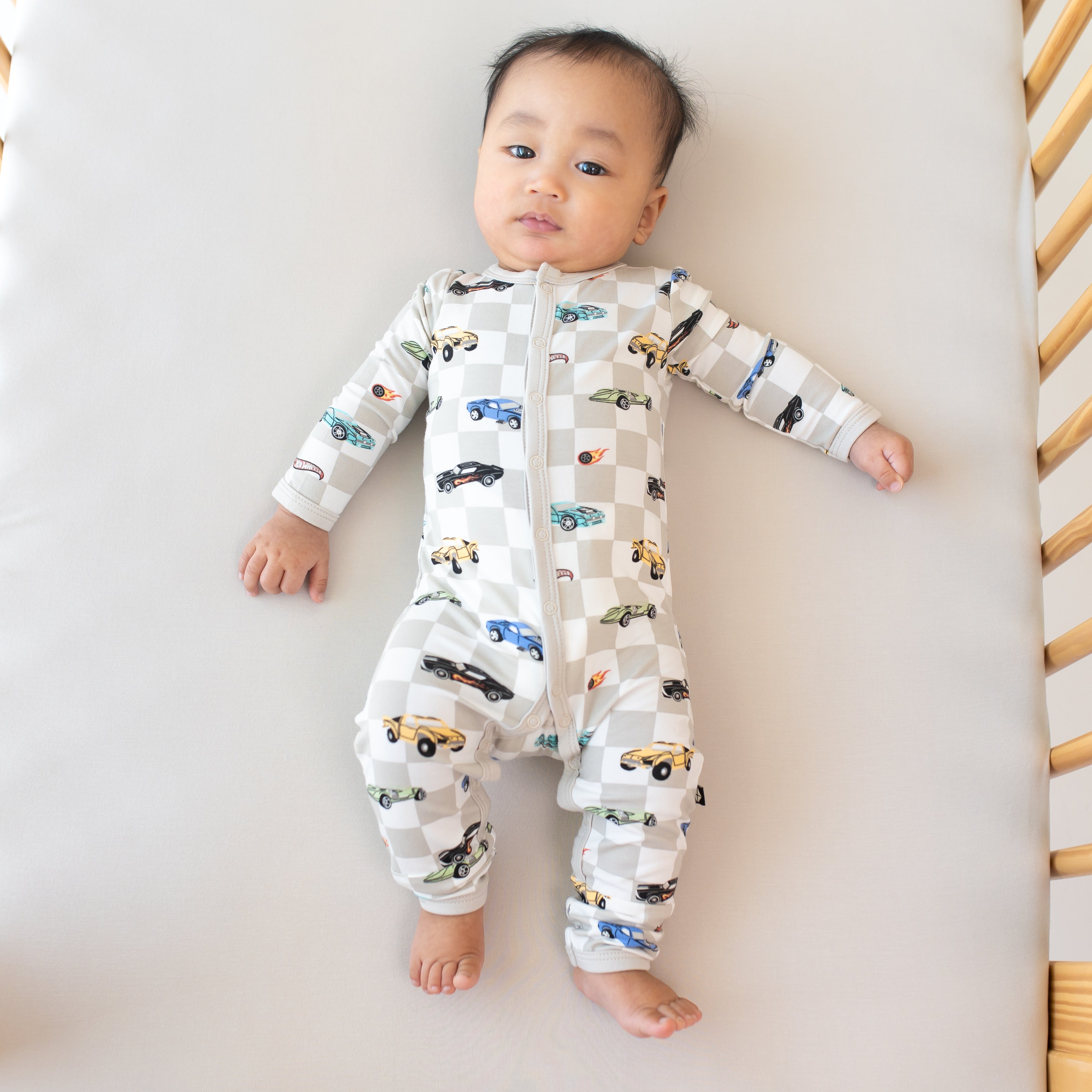 Infant laying in a crib on an Oat crib sheet wearing the Romper in Fast and Fierce