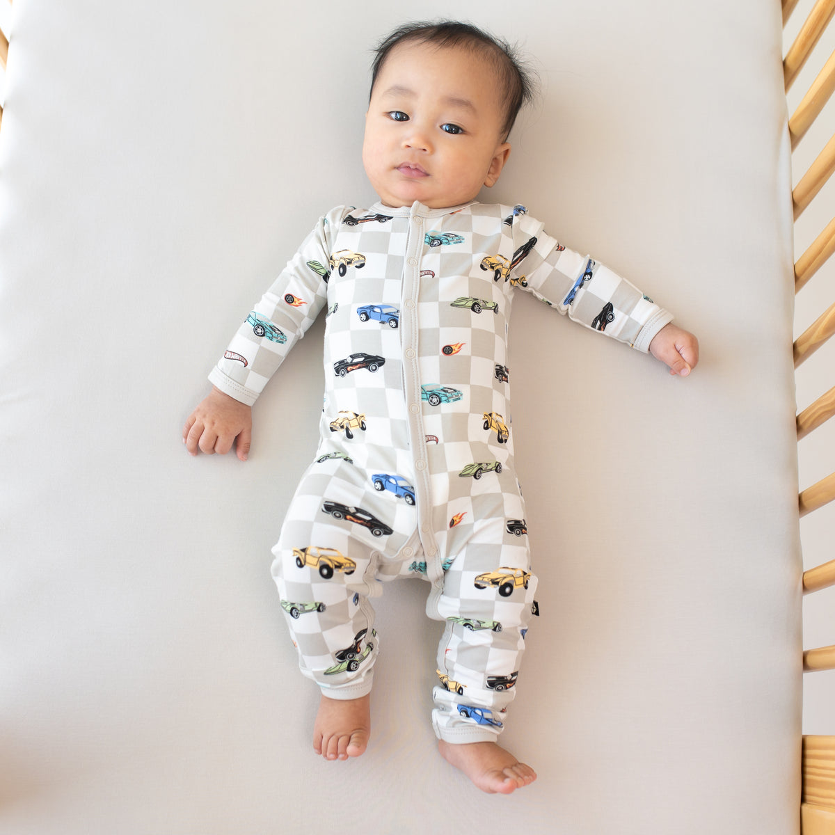 Infant laying in a crib on an Oat crib sheet wearing the Romper in Fast and Fierce