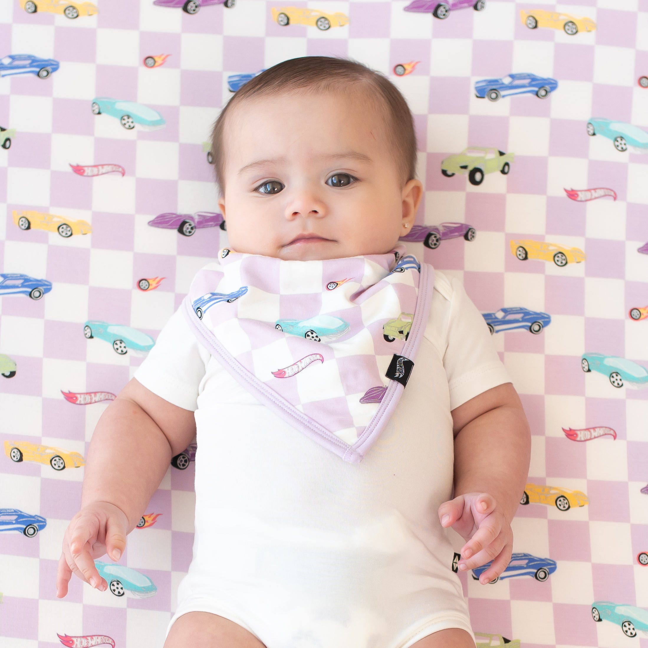 Infant wearing the Bib in Sparkles and Speed on a matching crib sheet wearing a short sleeve bodysuit in Cloud