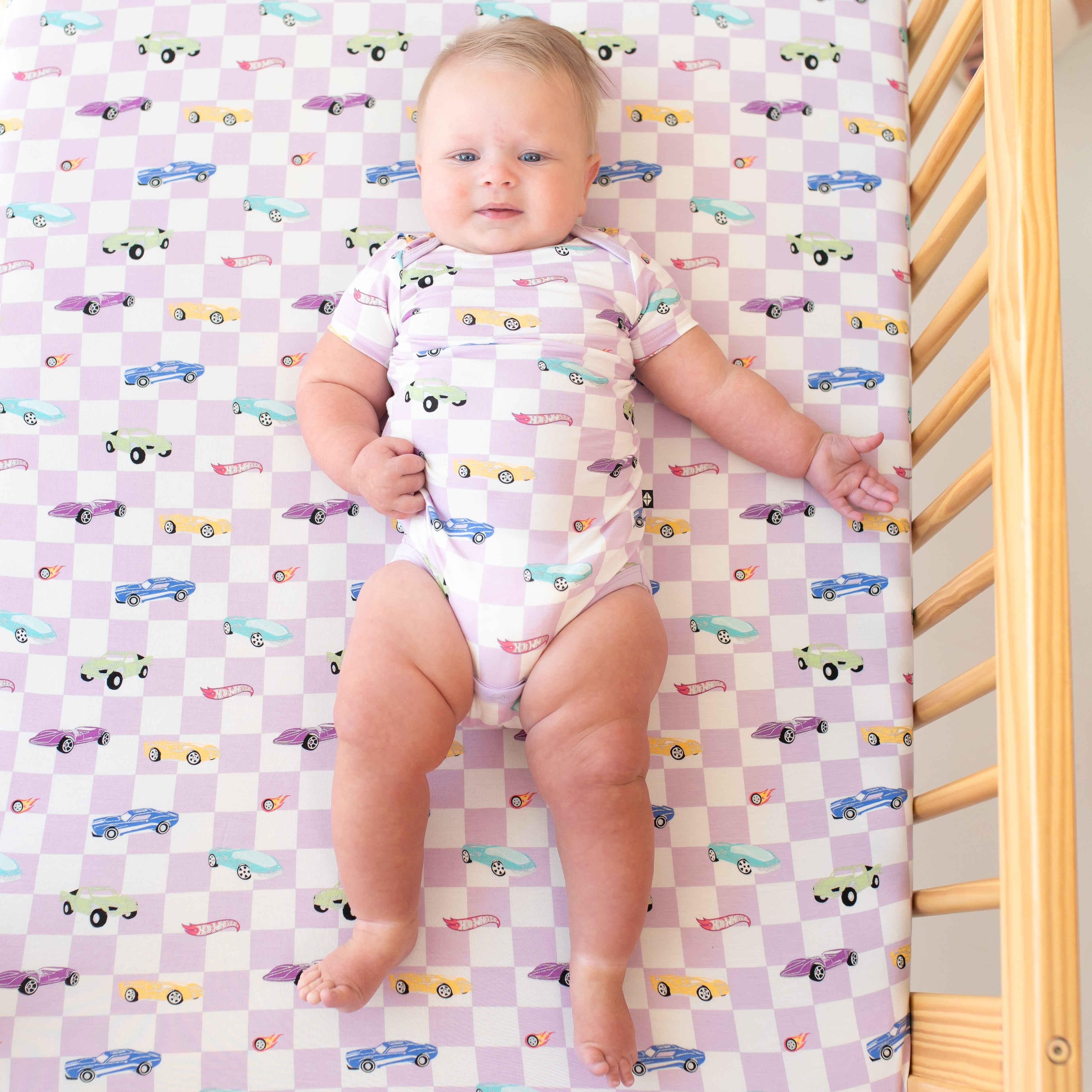 Infant wearing the Bodysuit in Sparkles and Speed laying in a crib on a matching Crib Sheet