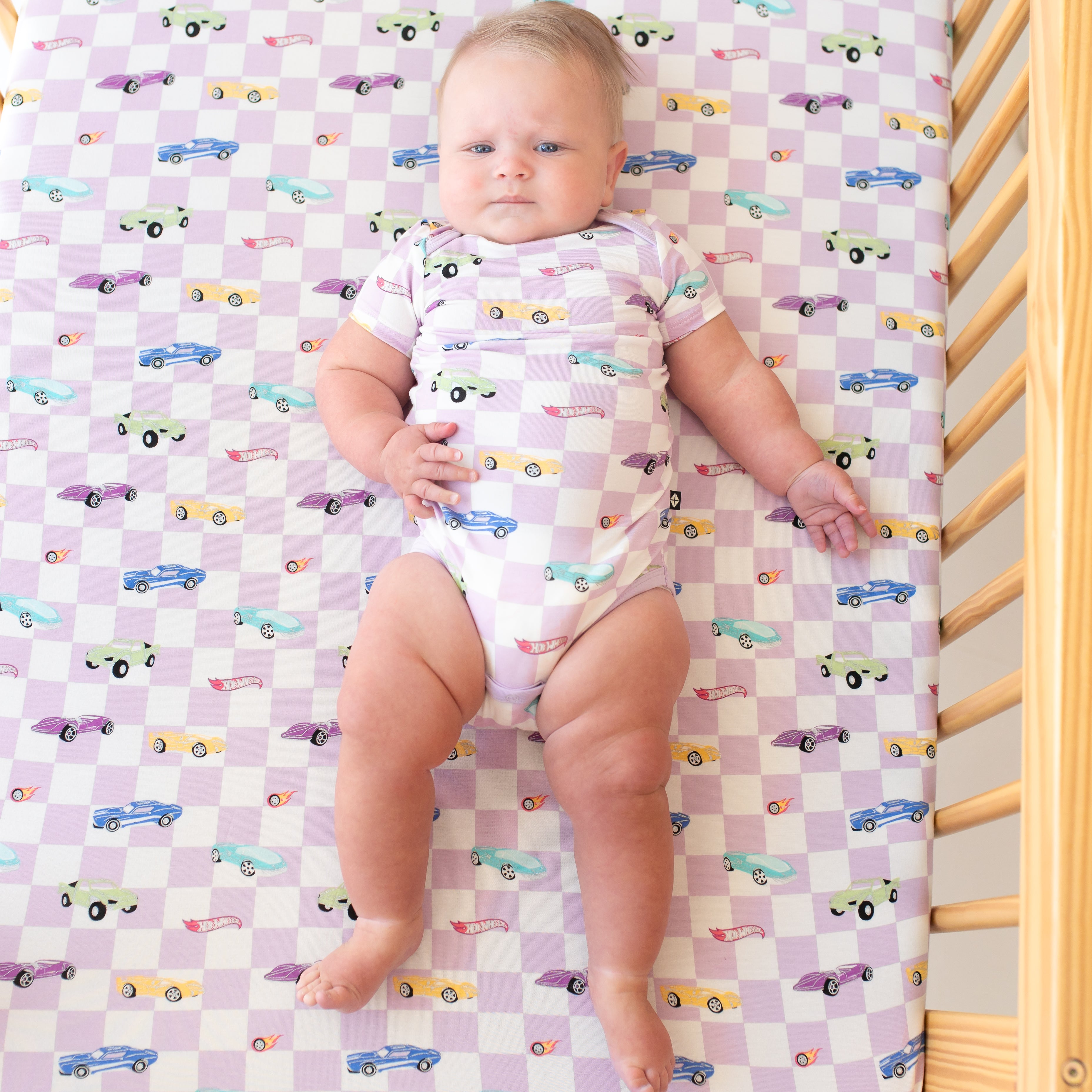 Infant laying in a crib on a Crib Sheet in Sparkles and Speed wearing a matching short sleeve bodysuit