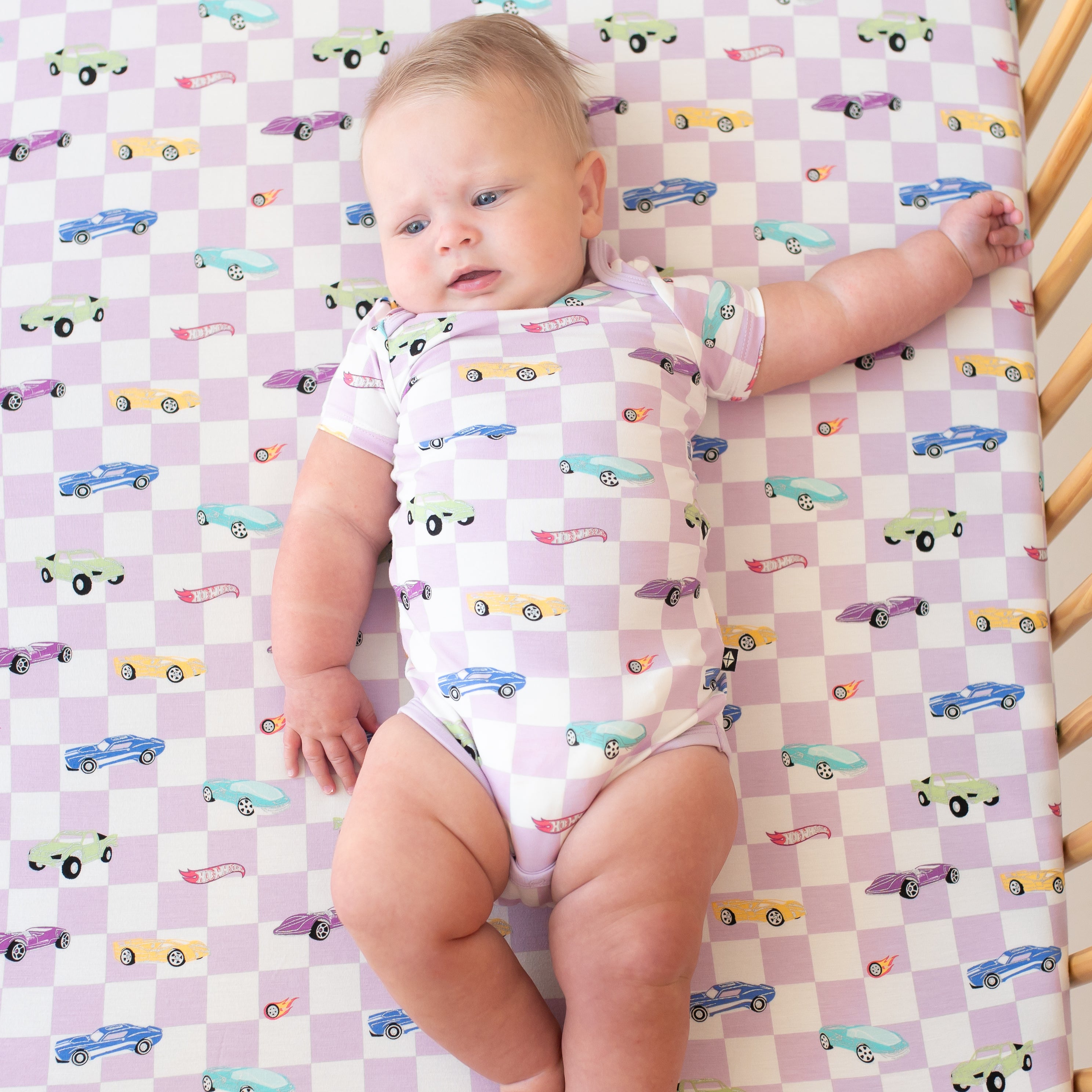 Infant earing the Bodysuit in Sparkles and Speed laying in a crib on a matching crib sheet