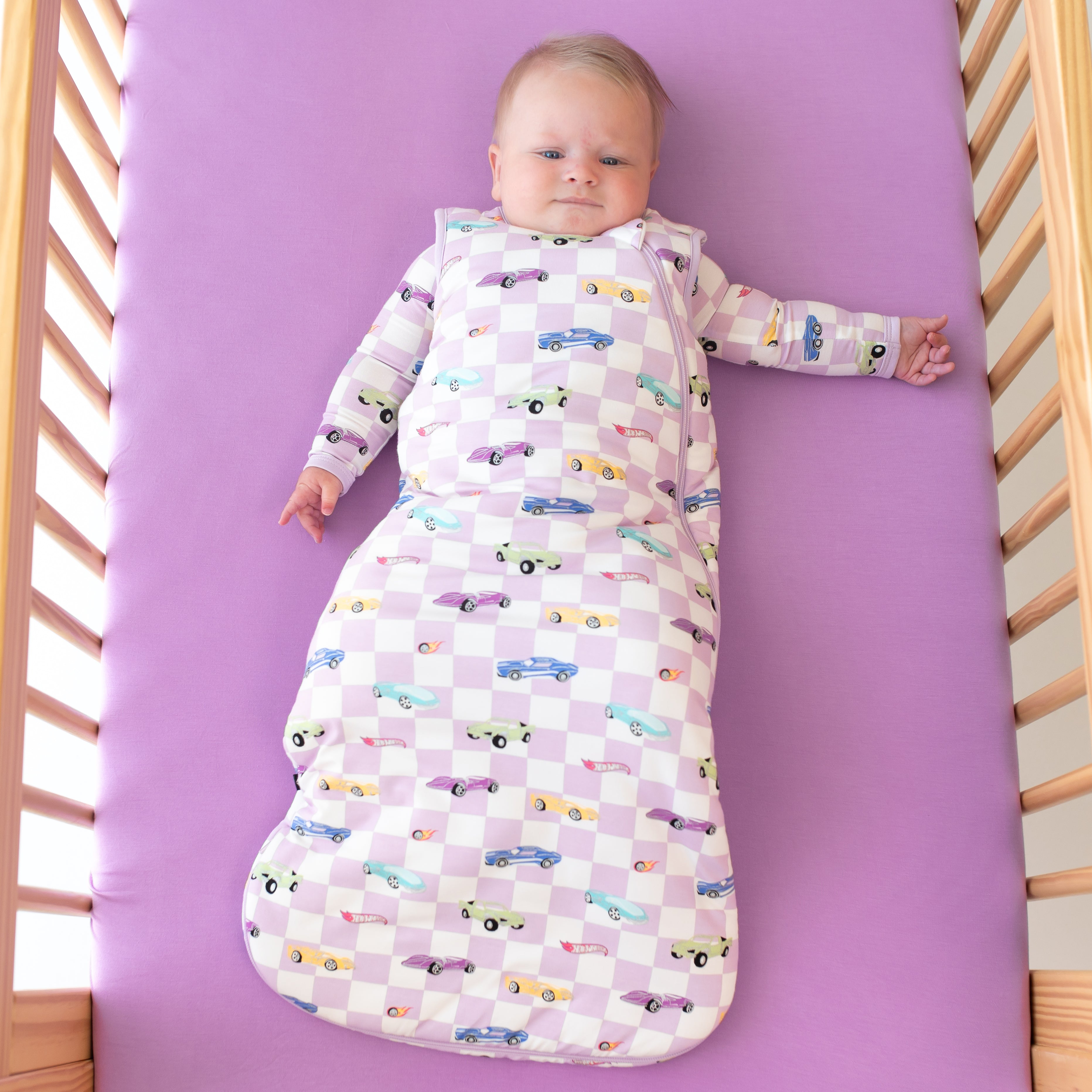 Infant laying on a Poi crib sheet wearing Hot Wheels Sleep Bag in Sparkles and Speed 2.5 with matching long sleeve pajamas
