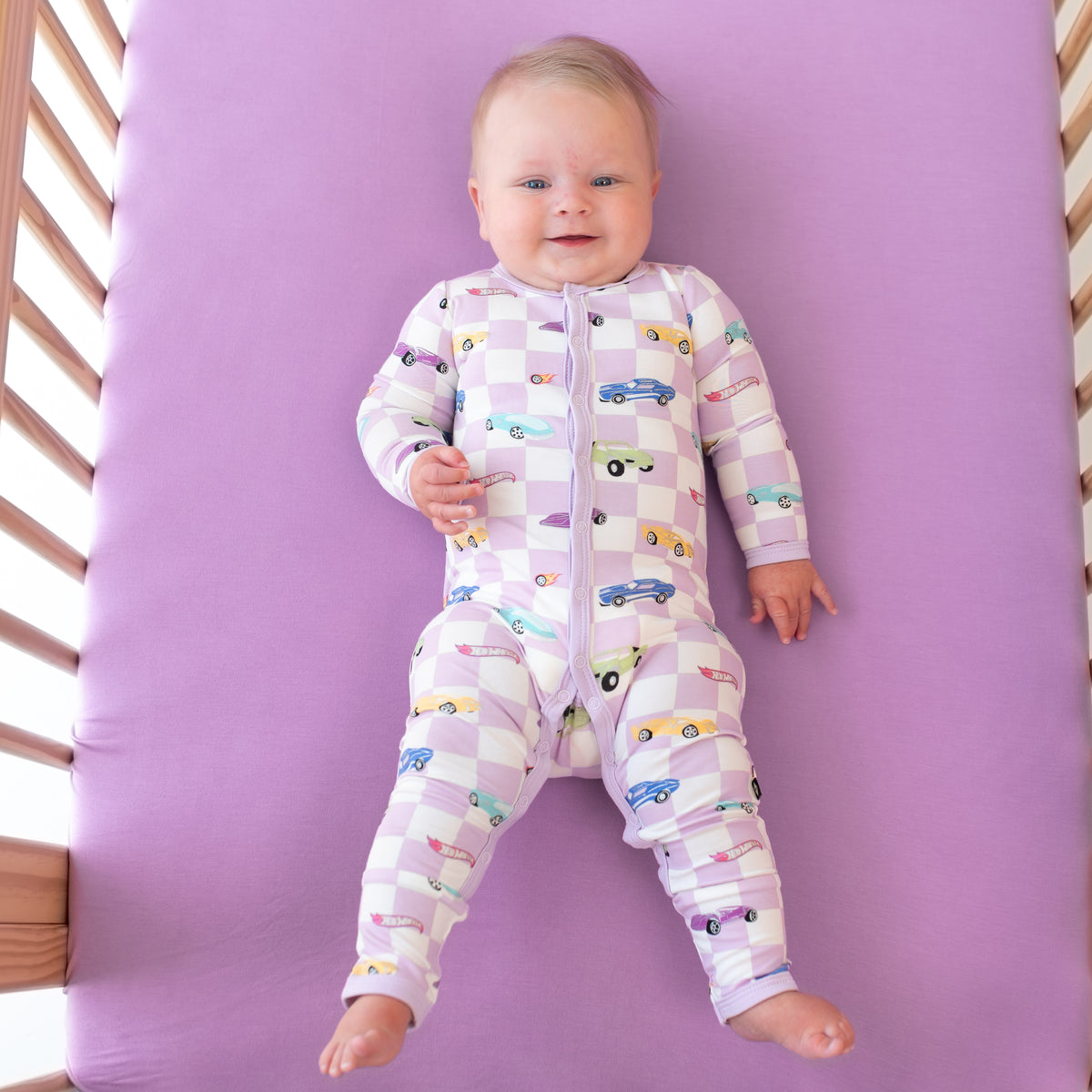 Infant laying on Poi Crib Sheet wearing snap Romper in Sparkles and Speed Hot Wheels print