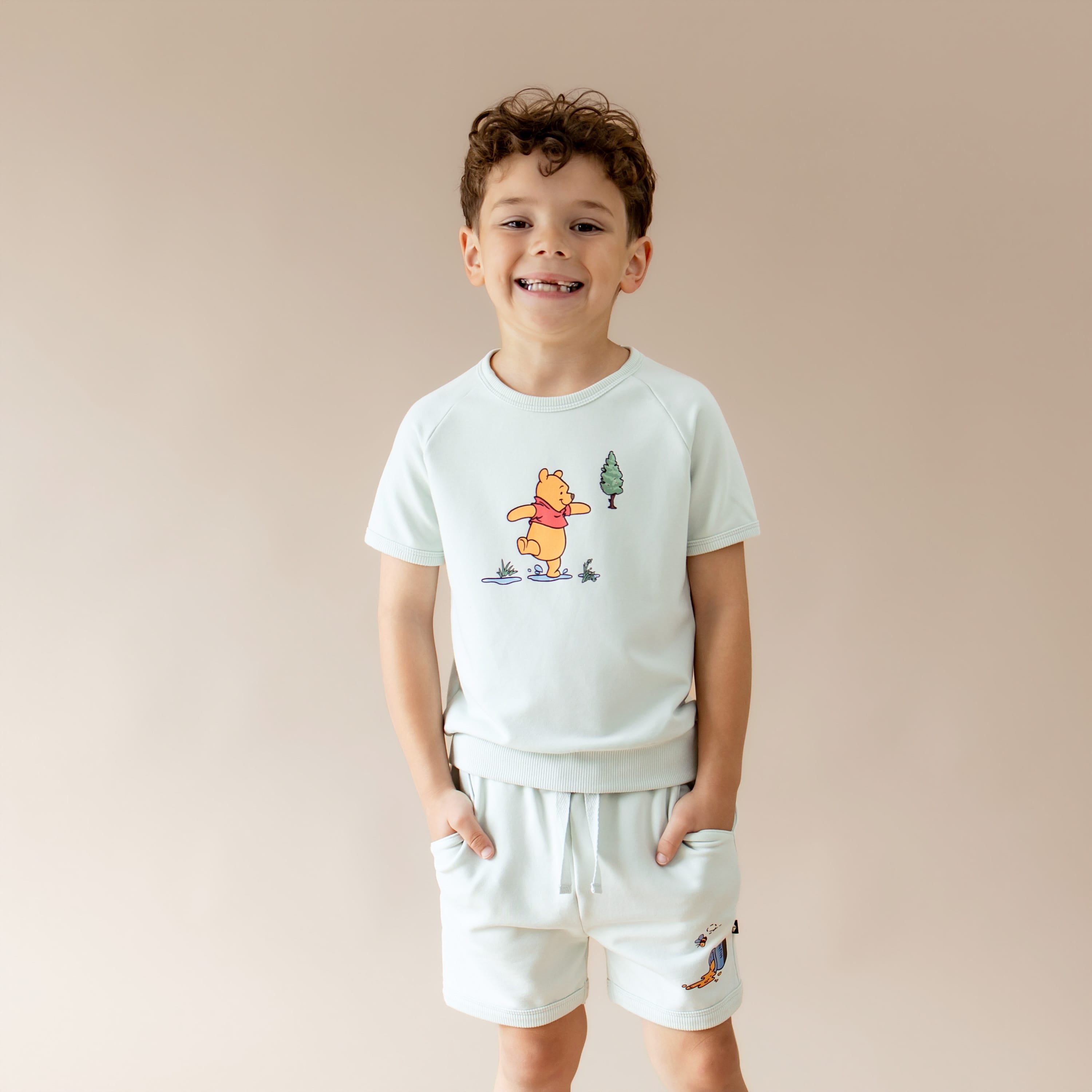 Young boy modeling the Short Sleeve Jogger Set in Winnie the Pooh on Dew with the hands in the shorts pockets