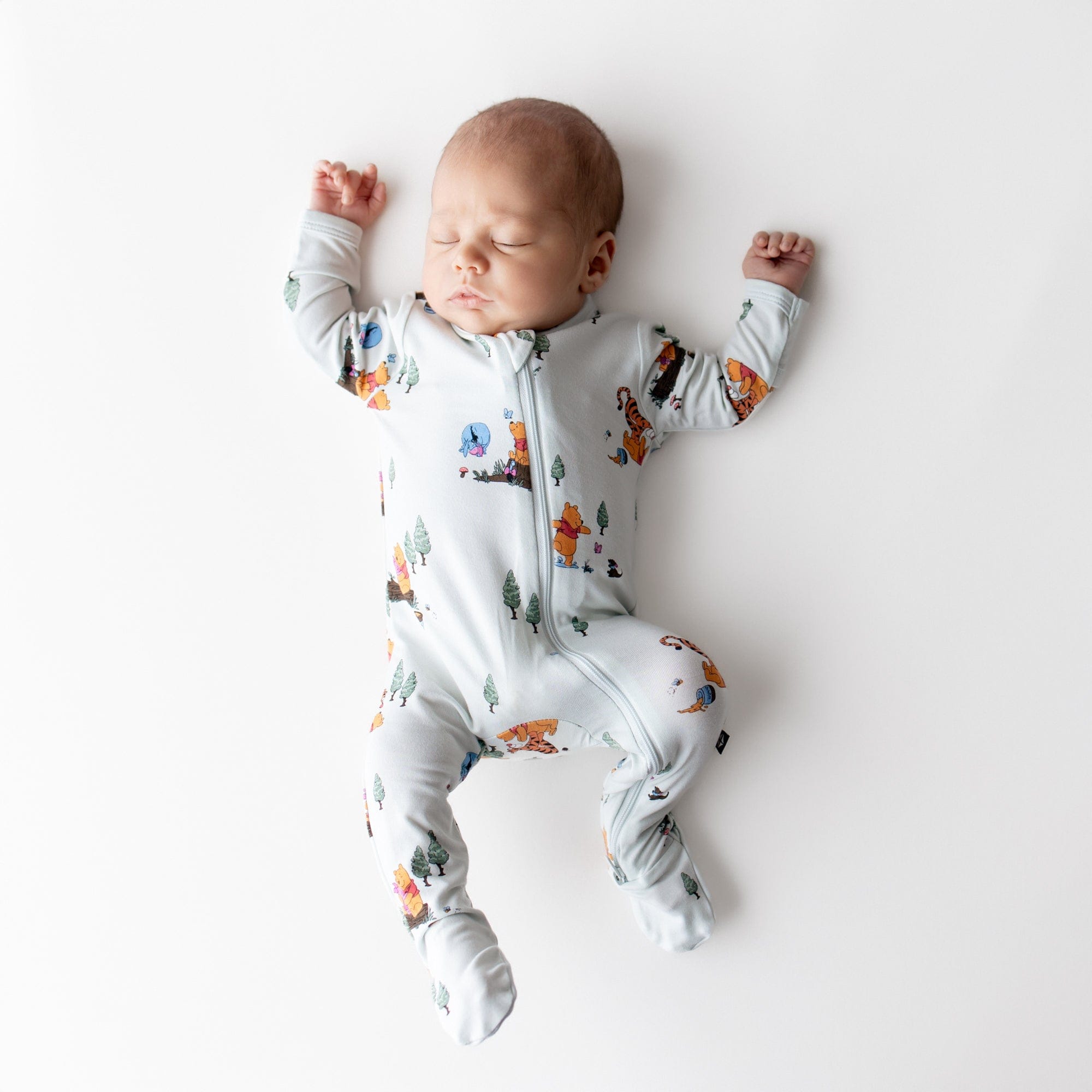 Sleeping newborn stretched out wearing the Zippered Footie in Winnie the Pooh Hundred Acre Wood