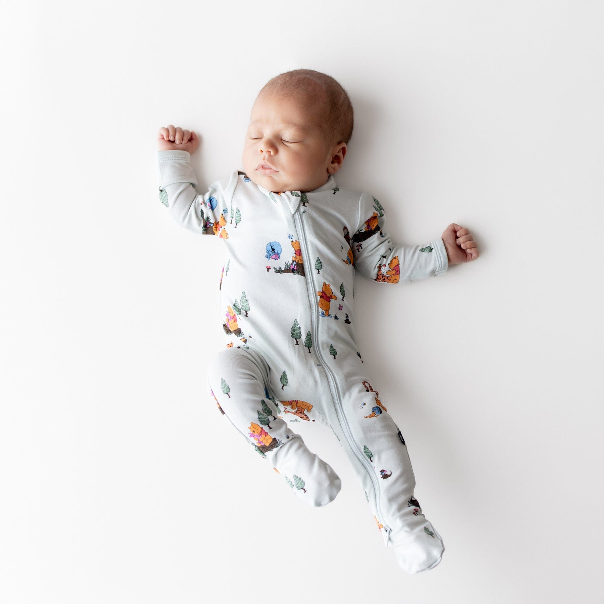 Sleeping newborn wearing the Zippered Footie in Winnie the Pooh Hundred Acre Wood