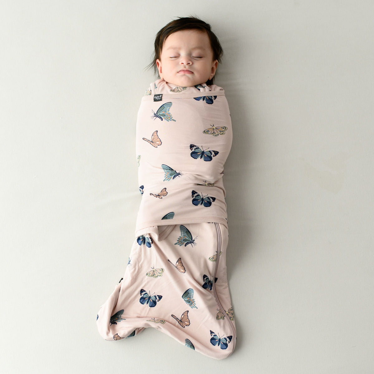 Infant model sleeping while swaddled in the 0.5 TOG Sleep Bag Swaddler in Blush Butterfly