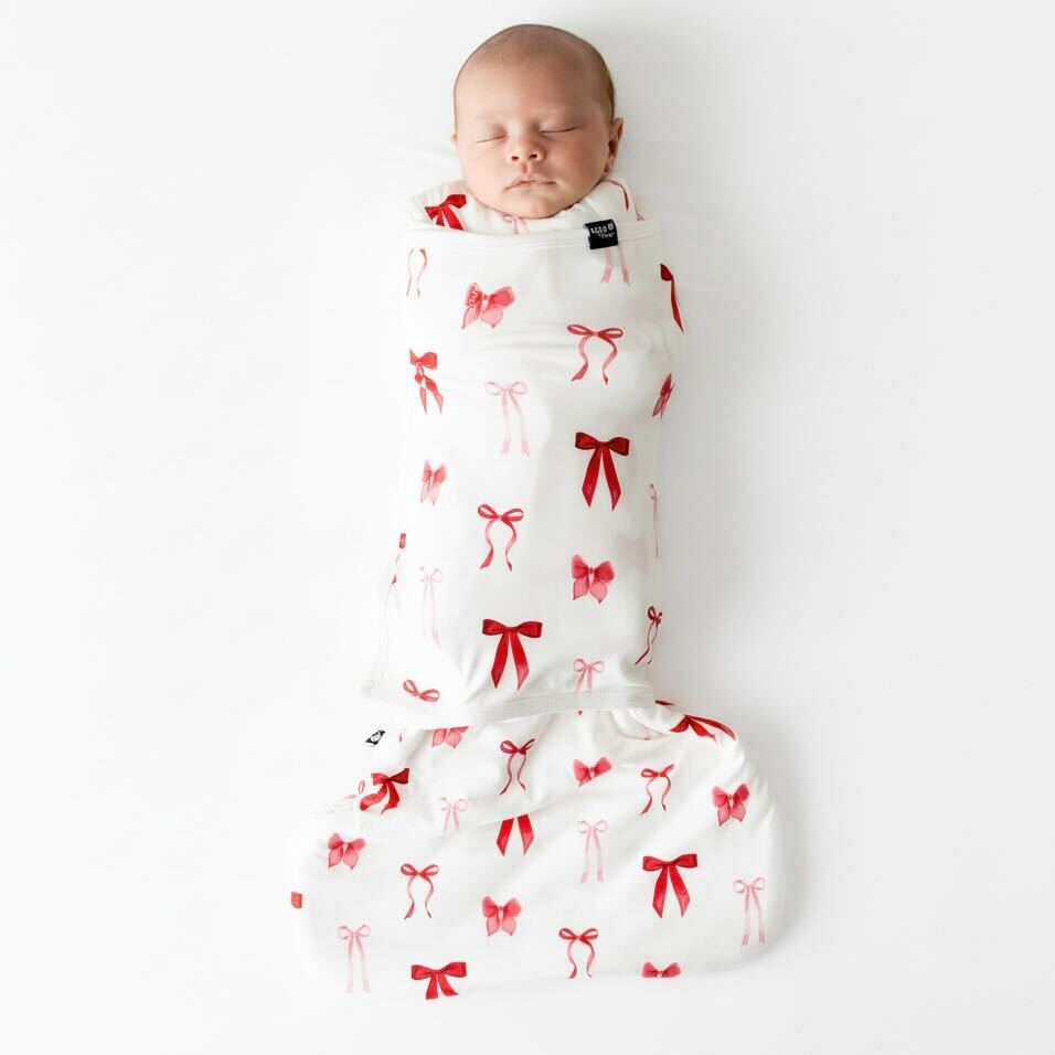 Baby asleep in a sleep bag swaddler that has a red and pink bow pattern