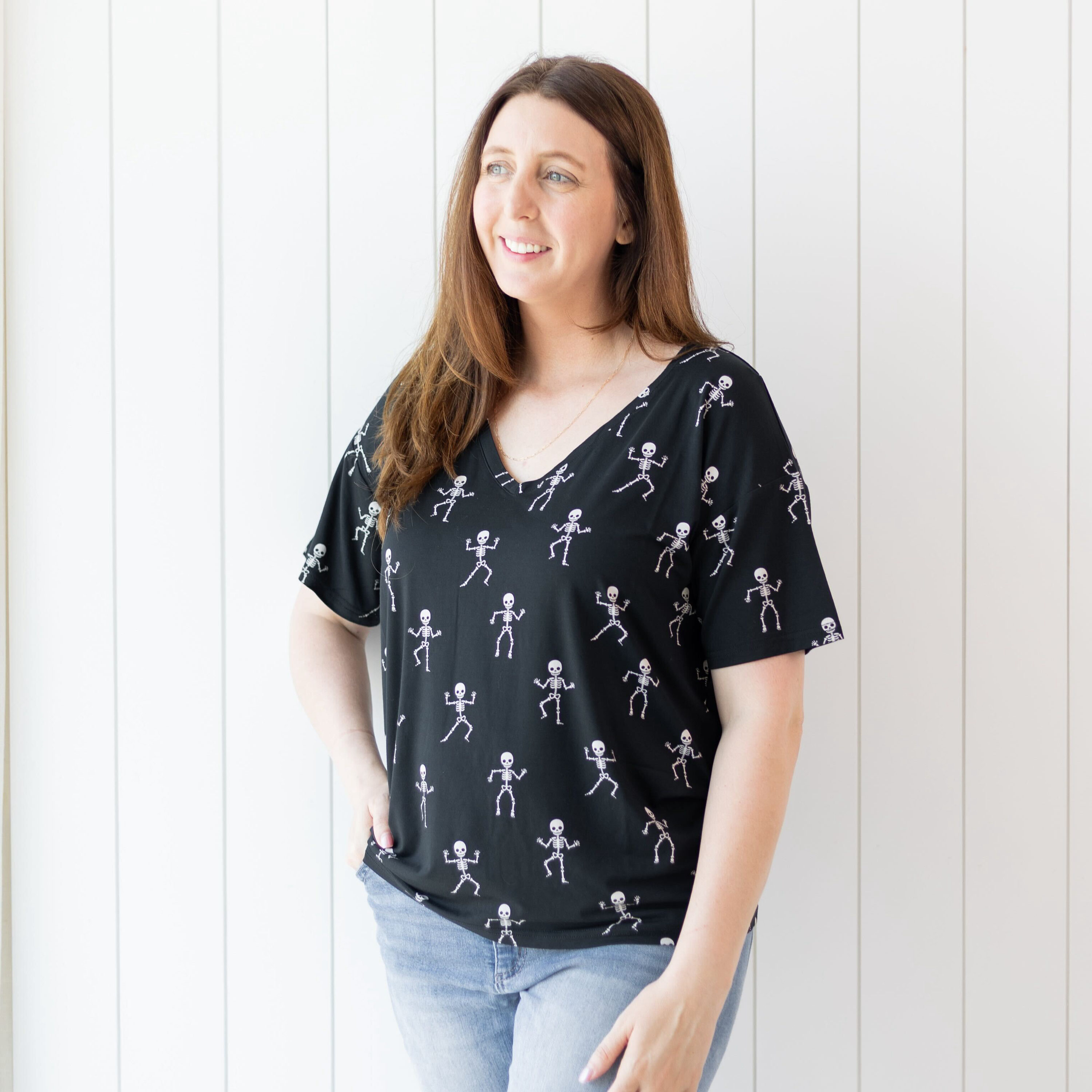 Female model standing in front of a white paneled wall looking off to the side wearing the Women's Relaxed Fit V-Neck in Skeleton with one hand in her jean front pocket