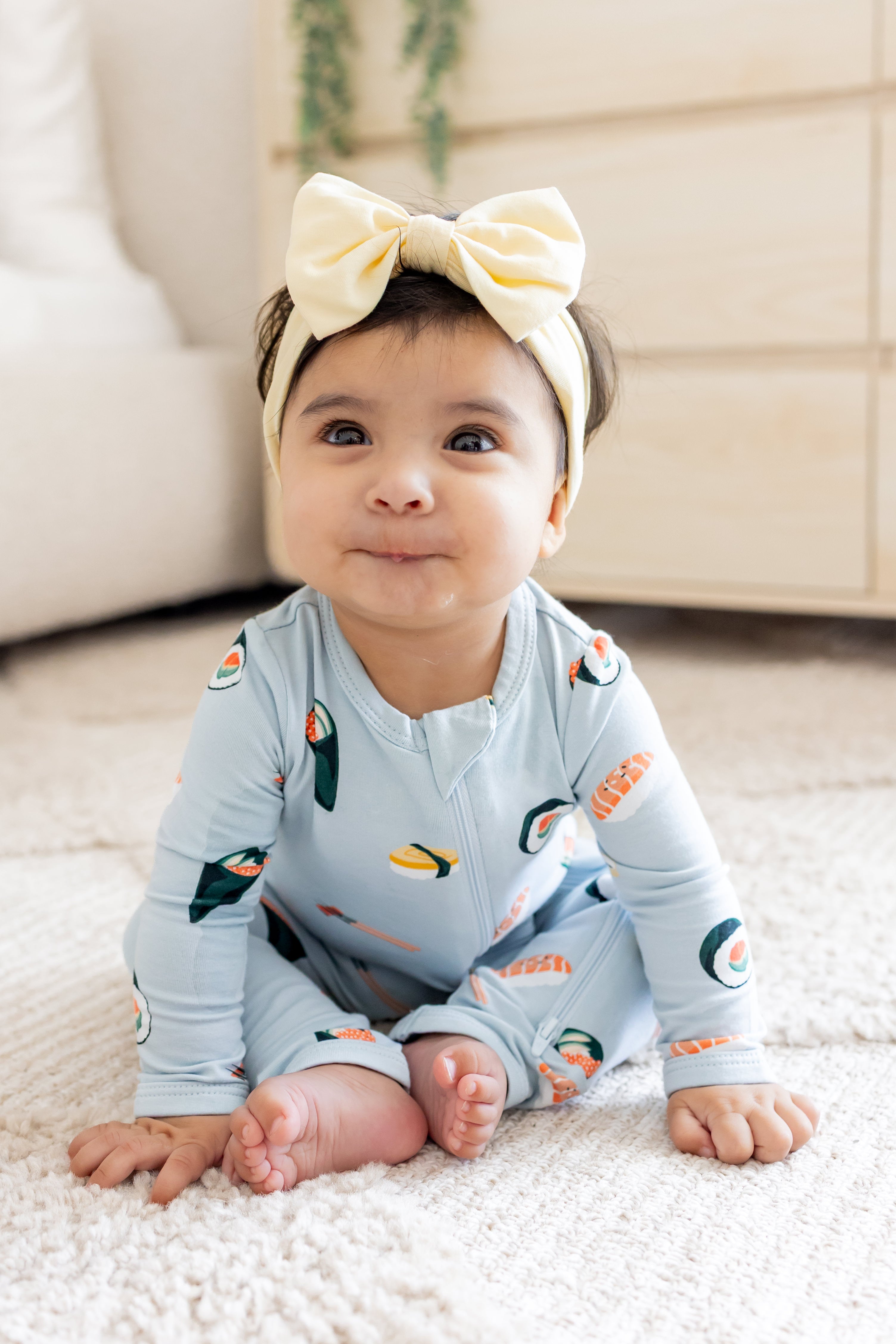 Baby sitting up leaned over in ice sushi zipper romper and yellow bow