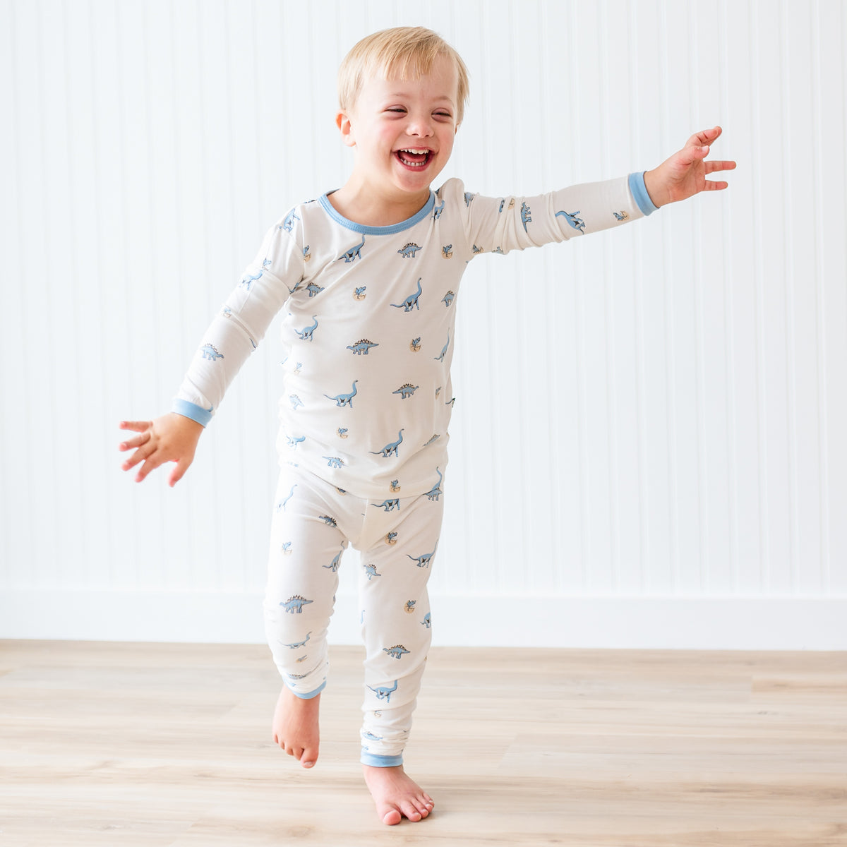 Child wearing a long-sleeve pajama set with dinosaur pattern on a light background