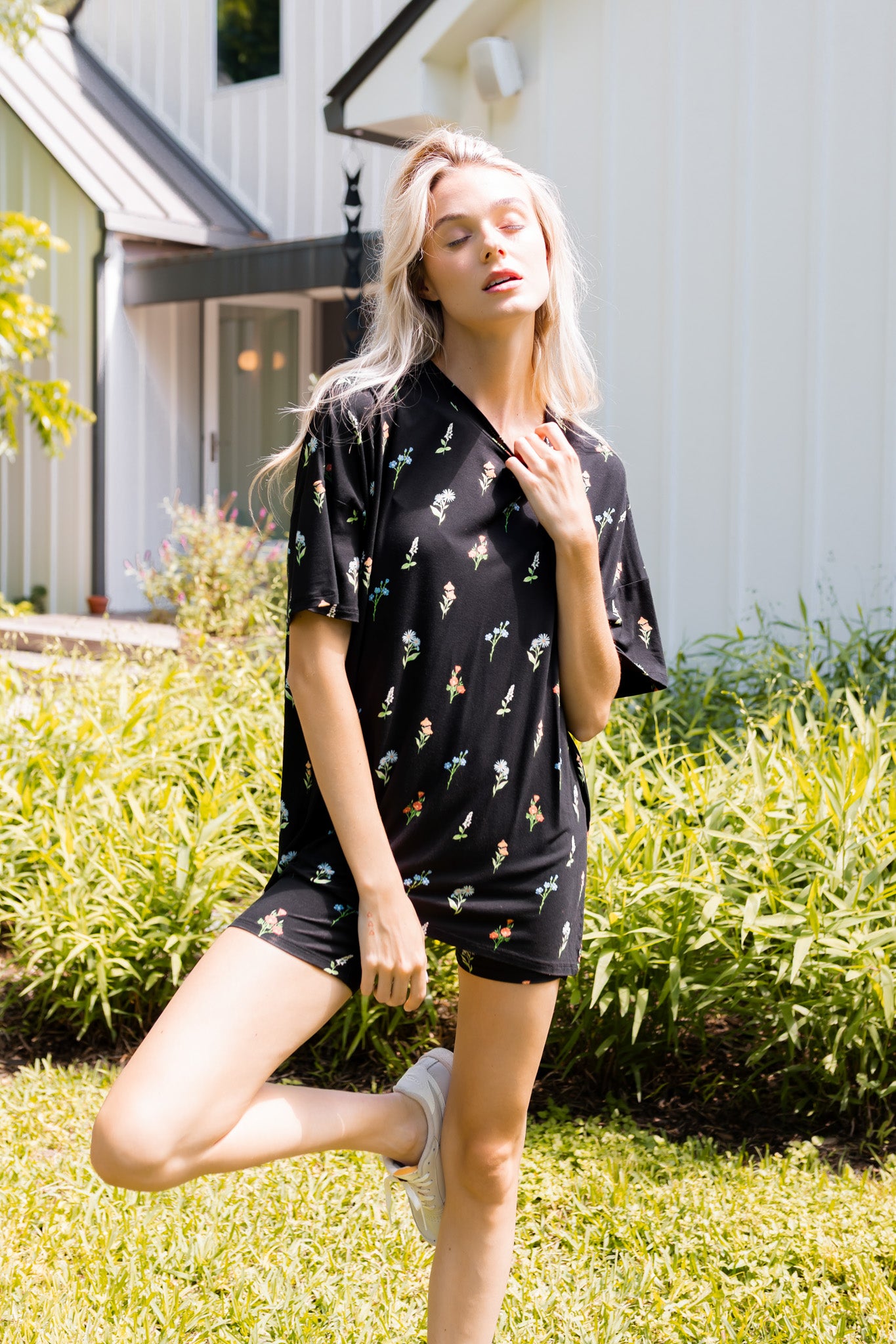 Model posing outdoors in sunlight wearing Women’s Biker Short Set in Midnight Wildflower print with bushes in the background